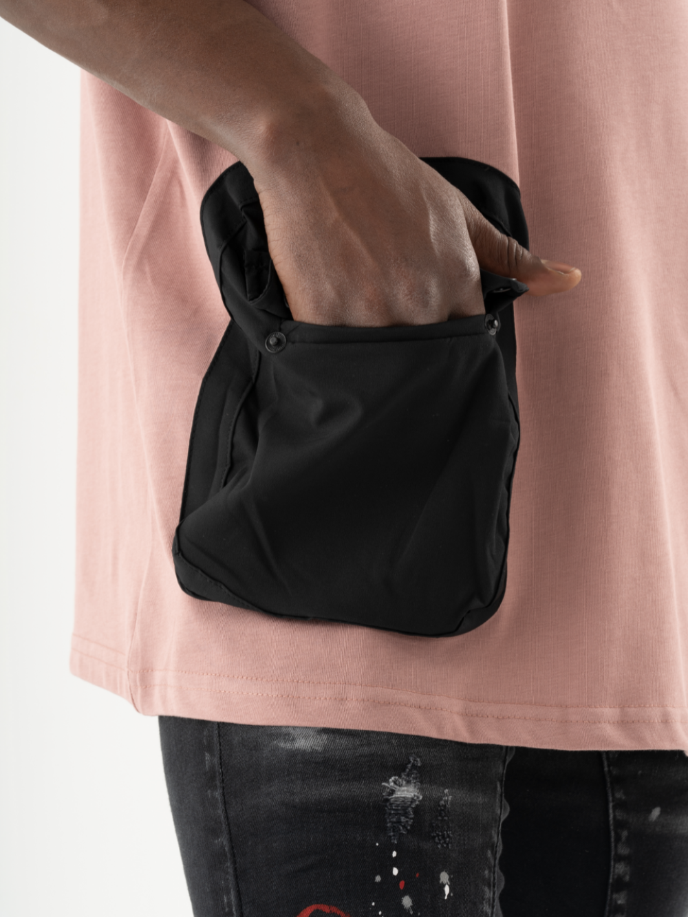 A person wearing a DUNE T-SHIRT and black jeans is shown placing their hand into a black buttoned front pocket.