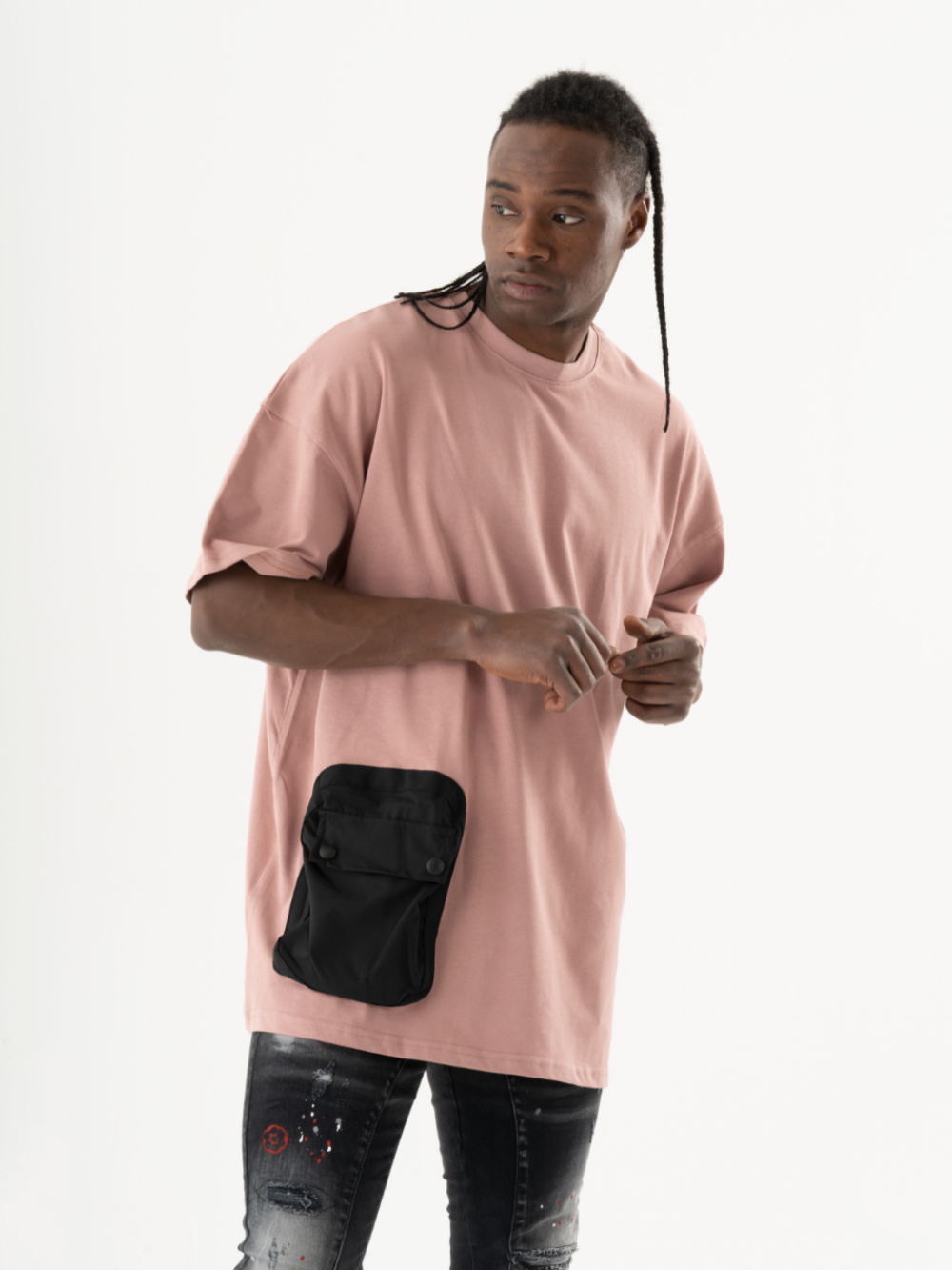 A person wearing a DUNE T-SHIRT with a black buttoned front pocket and distressed black jeans stands against a white background.