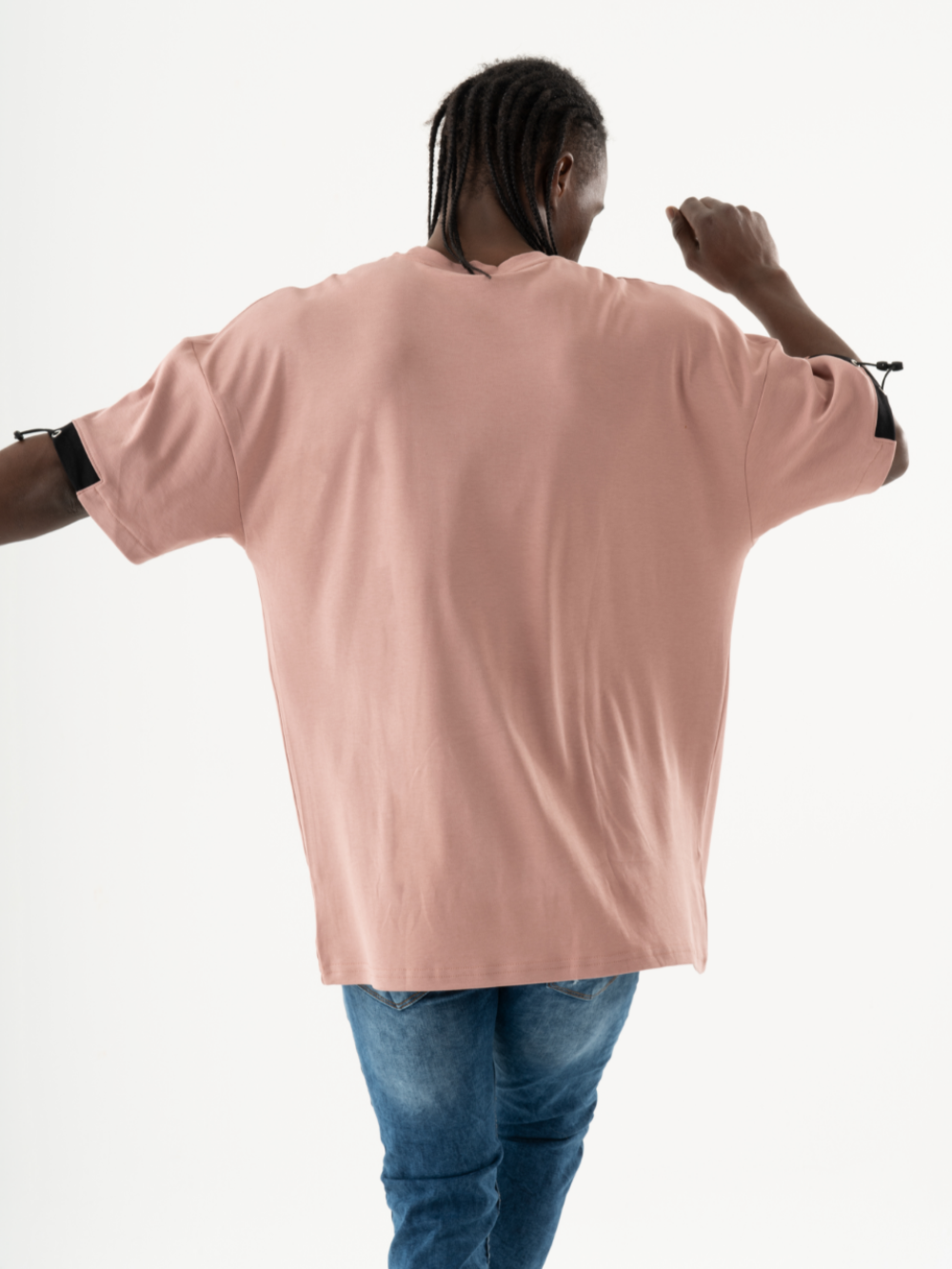 Person with braided hair wearing a salmon-colored, oversized KANGAROO T-SHIRT and blue jeans seen from the back walking away.
