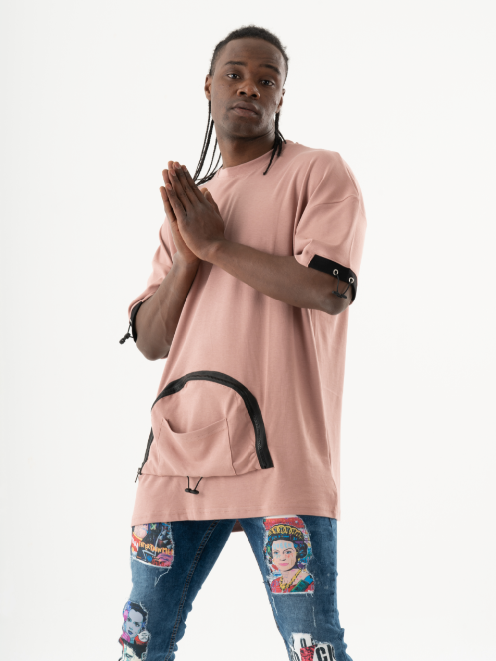 A person in a KANGAROO T-SHIRT, patterned jeans, and braided hair poses with hands together against a plain white background.