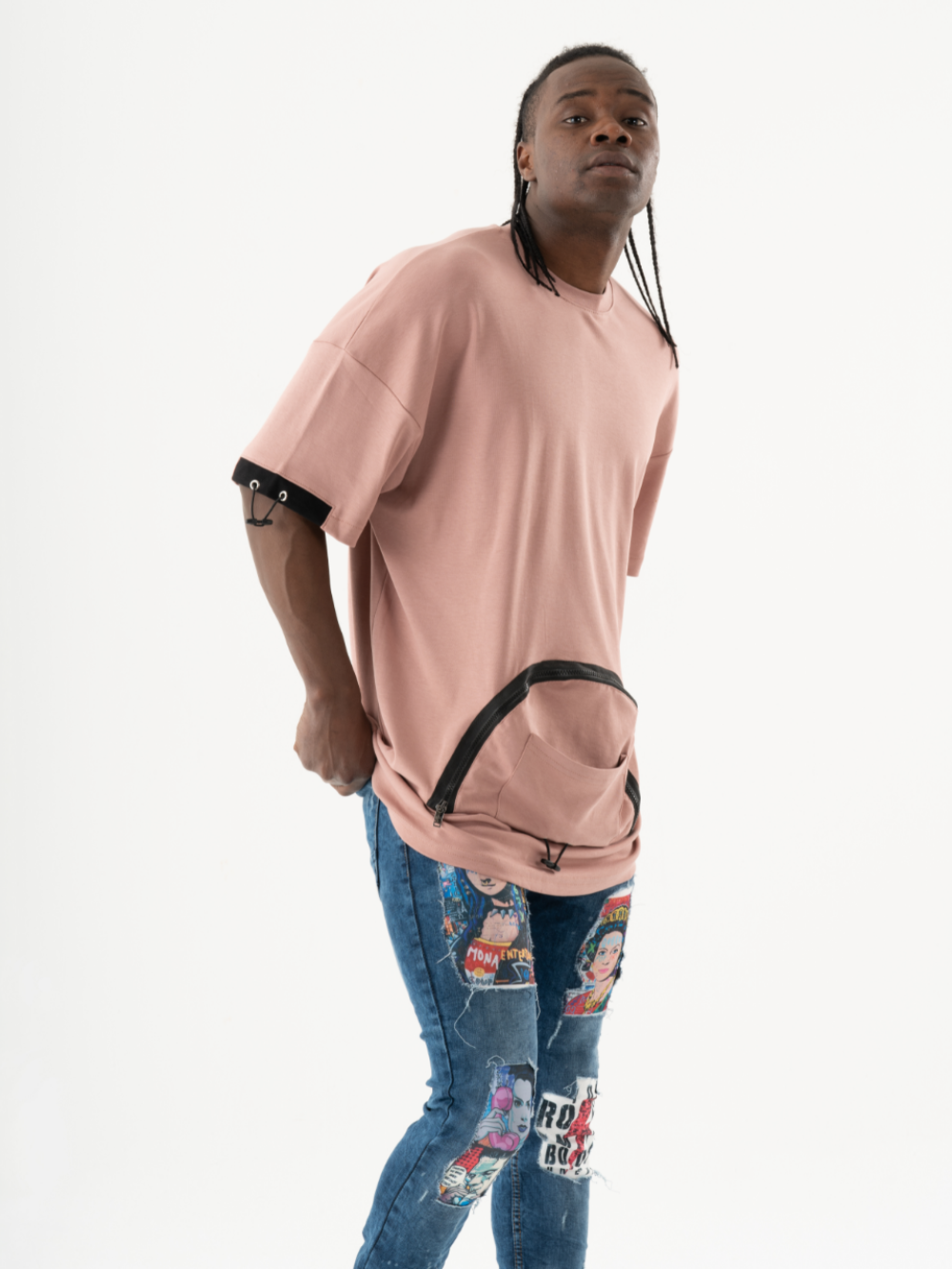 A person with long braided hair wears a KANGAROO T-SHIRT with black accents and blue jeans featuring vibrant patches and graphics, posing against a plain white background.