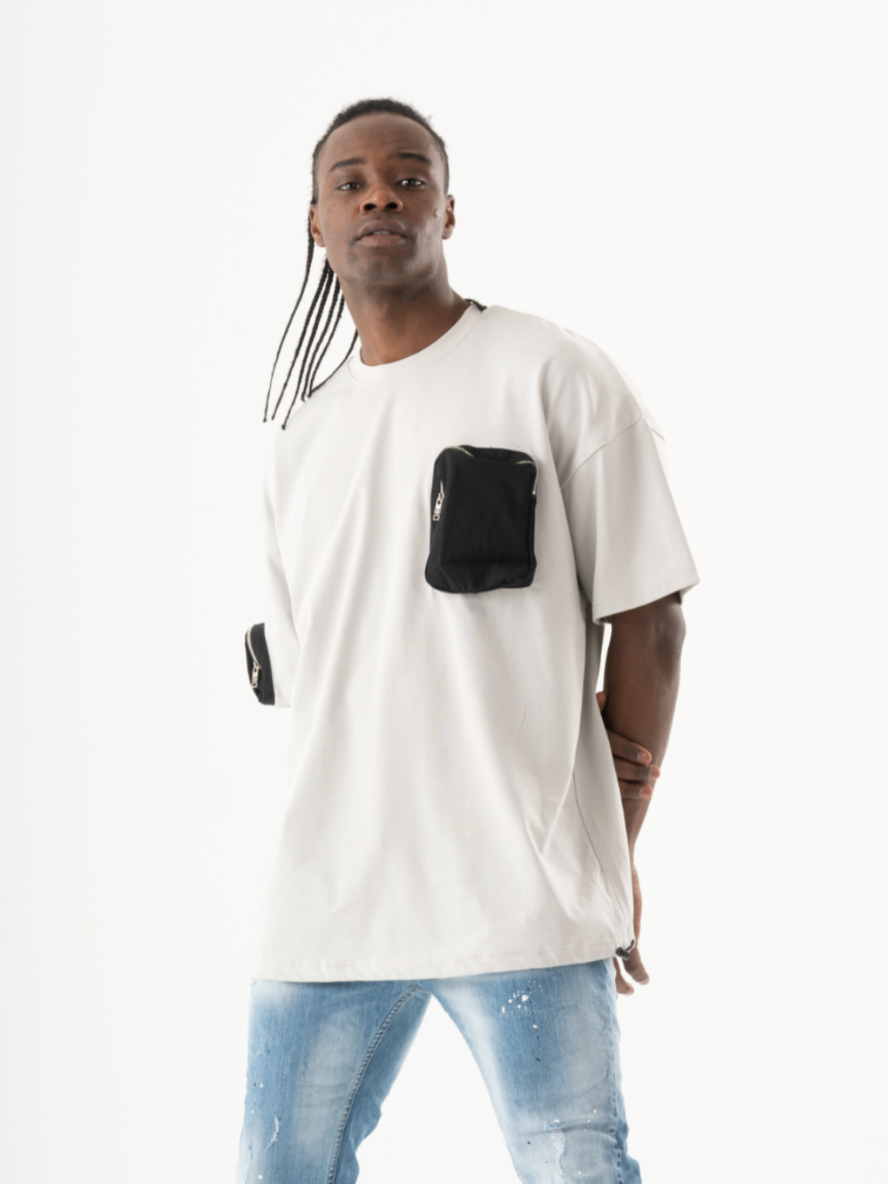 Man with long braided hair wearing a KLOUD T-SHIRT and blue jeans stands against a white background, showcasing his casual look.