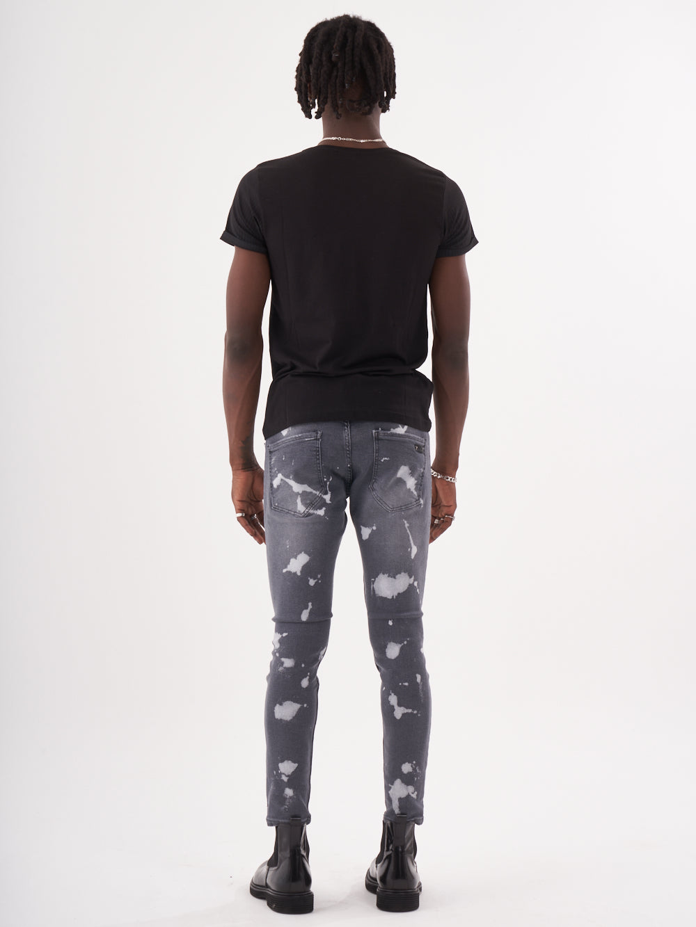 The back view of a man wearing a MAVERICK t - shirt and grey tie dye jeans.