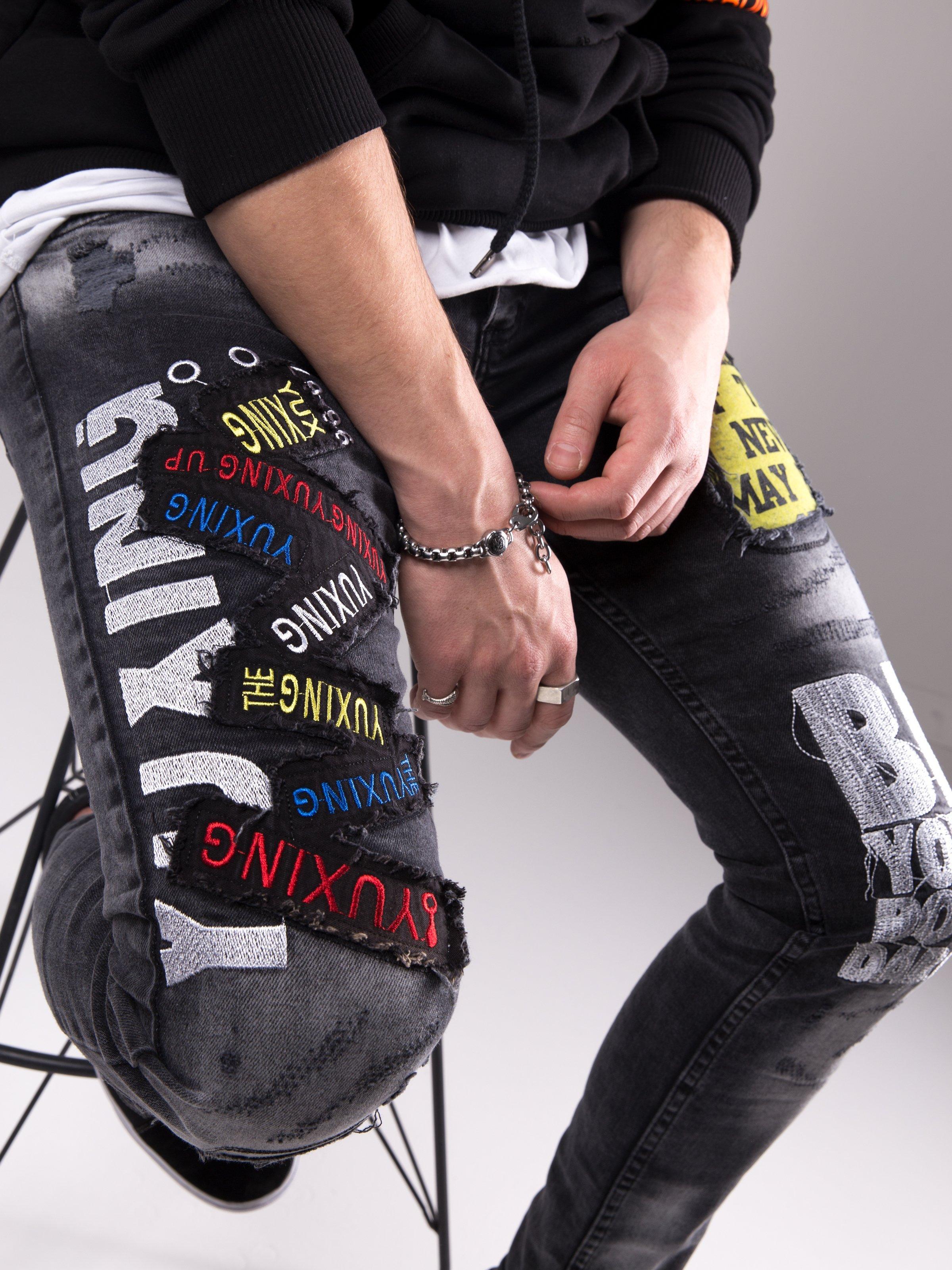 A man wearing a pair of Savage Secret jeans with embroidered words on them.