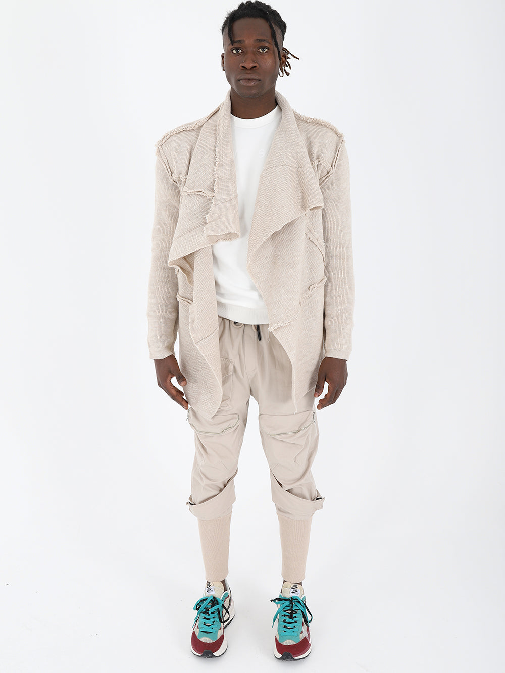 A man wearing the ASYMMETRIC SHORT CARDIGAN // IVORY jacket and sneakers.