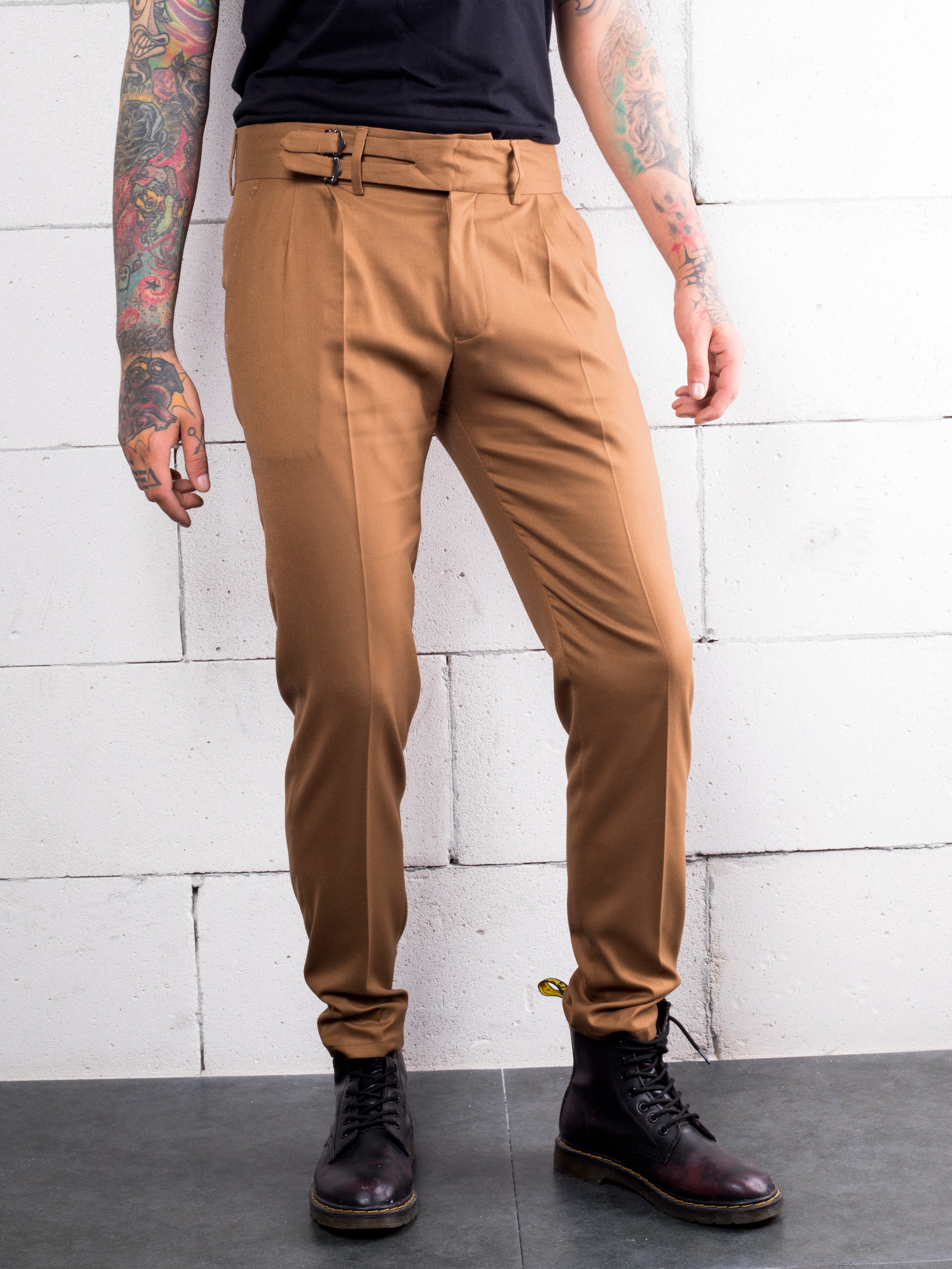 A man with tattoos wearing cotton-stretch tan slacks from Los Angeles carrying a CROISSANT.