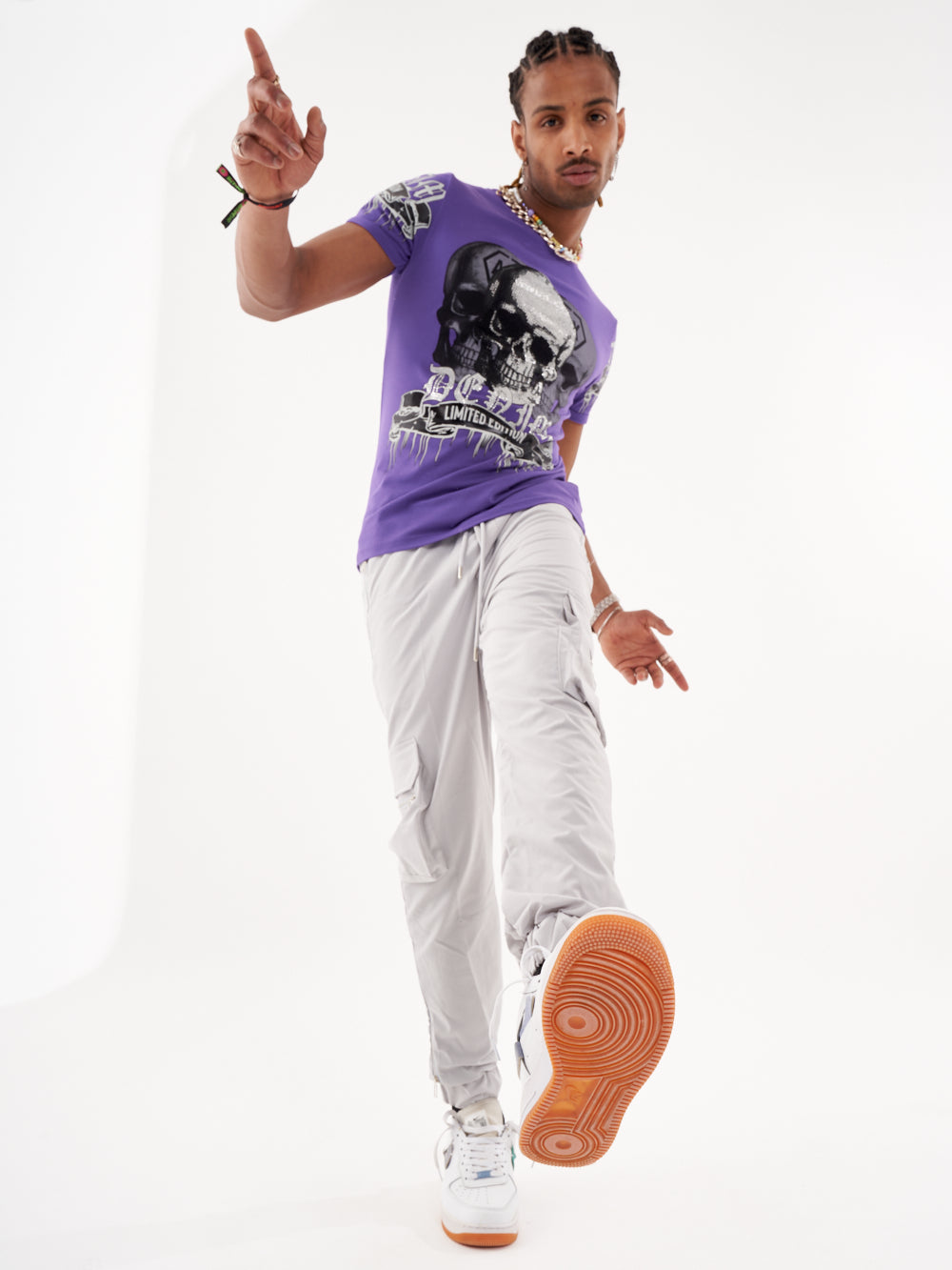 A man wearing a SKULL CRUSHER T-SHIRT | PURPLE and grey pants.