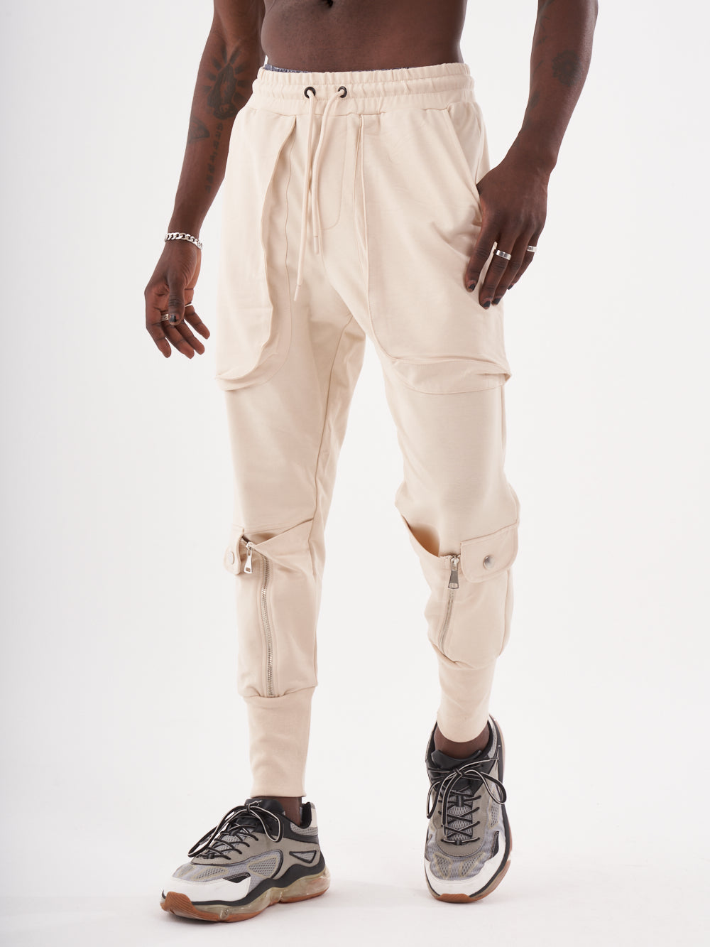 A man wearing GUERRILLA | BEIGE sweatpants and sneakers.