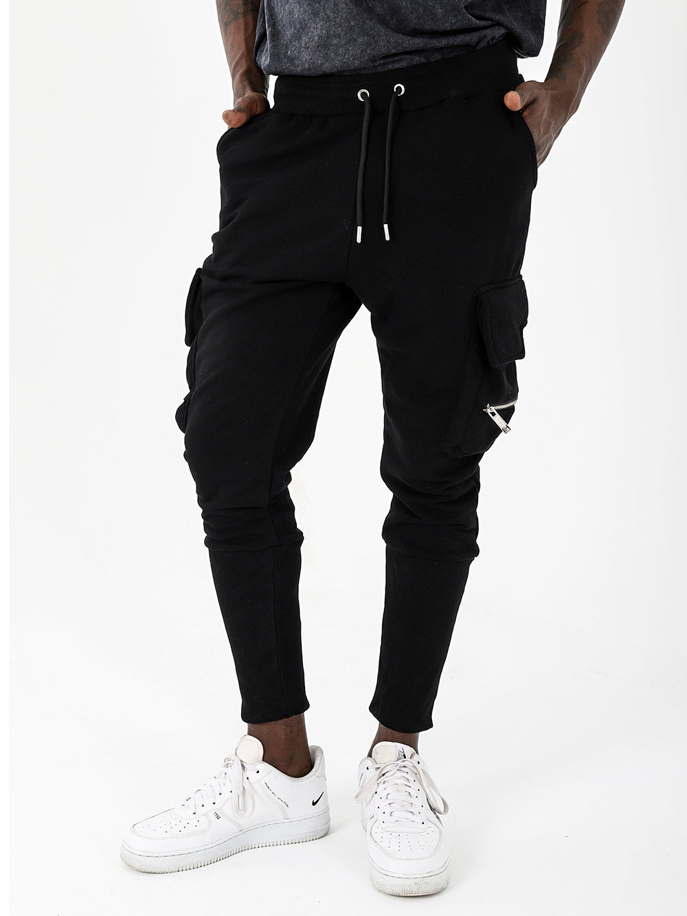 A man wearing comfortable black RAMBO JOGGERS cargo pants with plenty of pockets, paired with white sneakers.