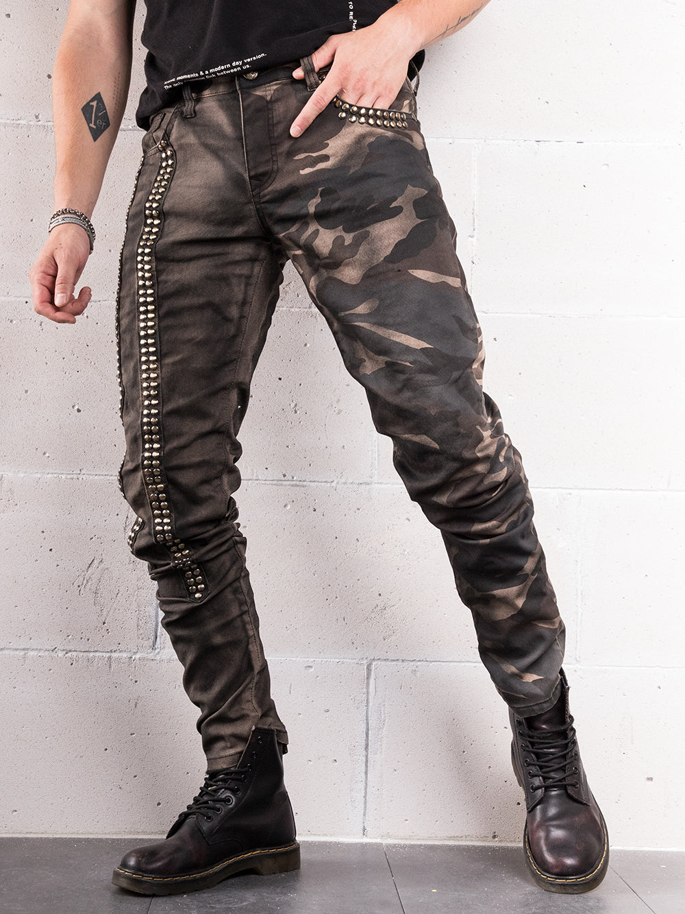 A man wearing a pair of SNIPER skinny fit black jeans and a black t-shirt OR A man wearing SNIPER black jeans with hand crafted details and a black t-shirt made from elastic fabric.