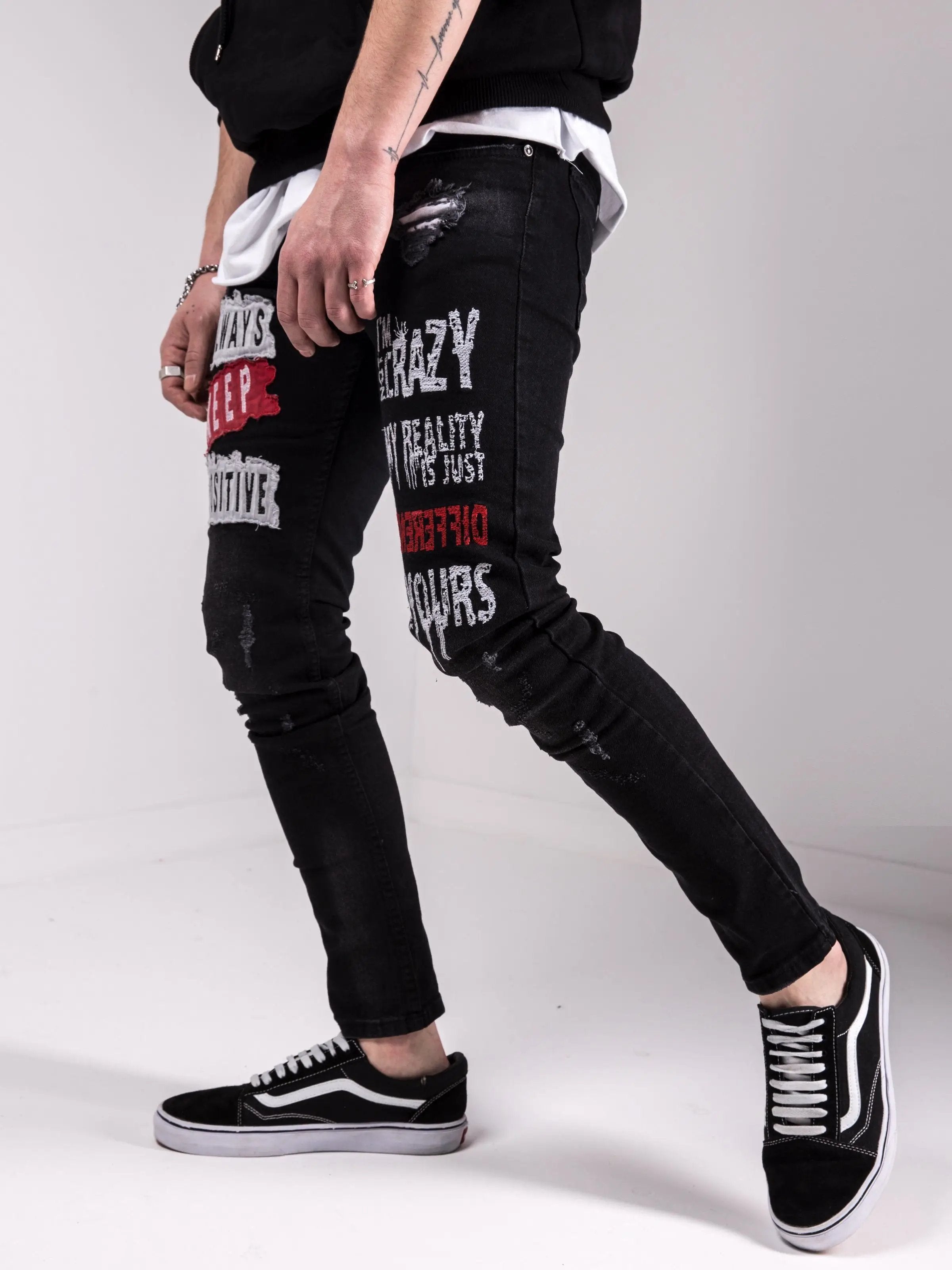 A man wearing a pair of black I'M NOT CRAZY jeans and a pair of I'M NOT CRAZY sneakers.