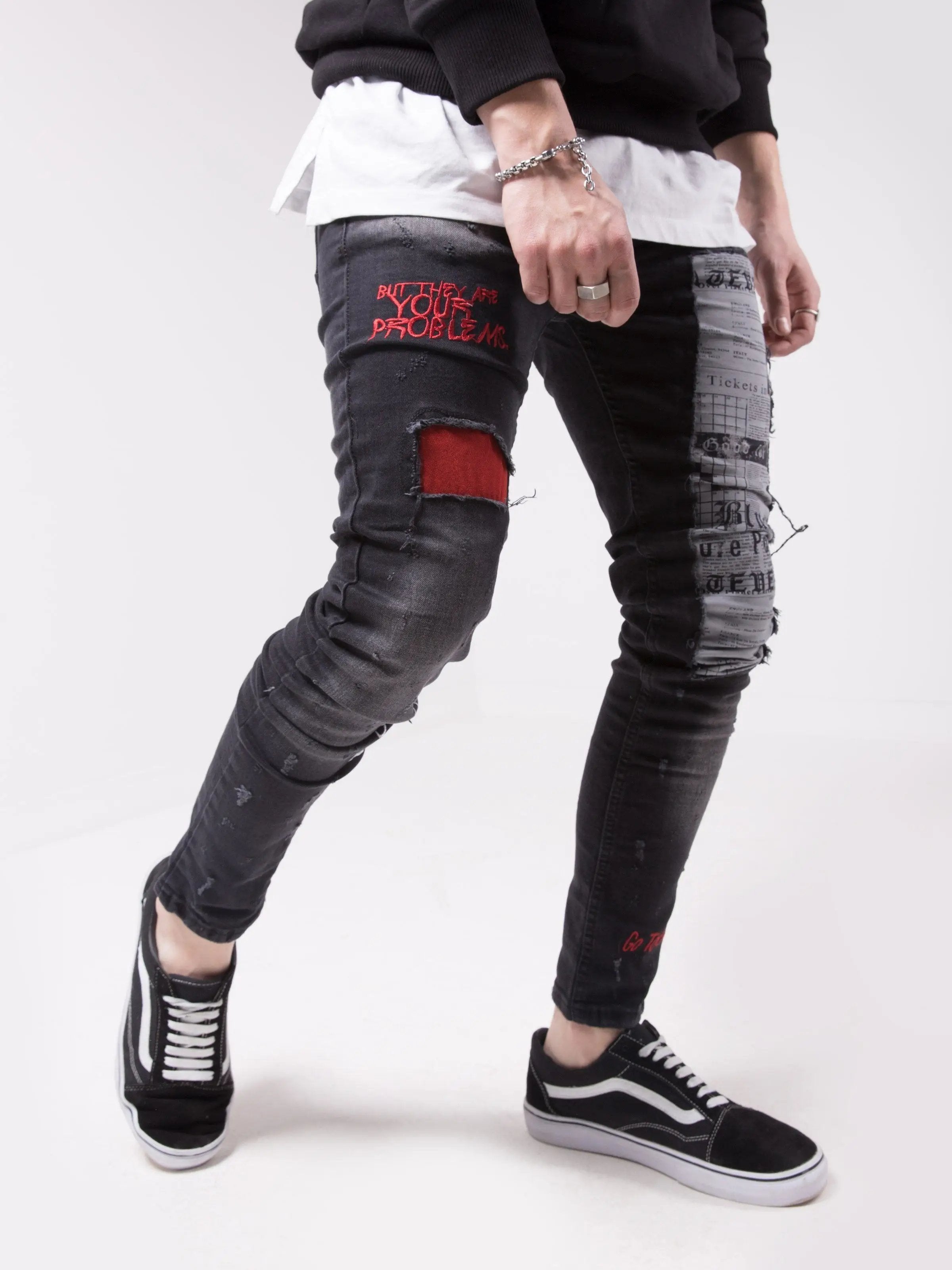 A man wearing a pair of black SKYSCRAPER jeans with red patches.