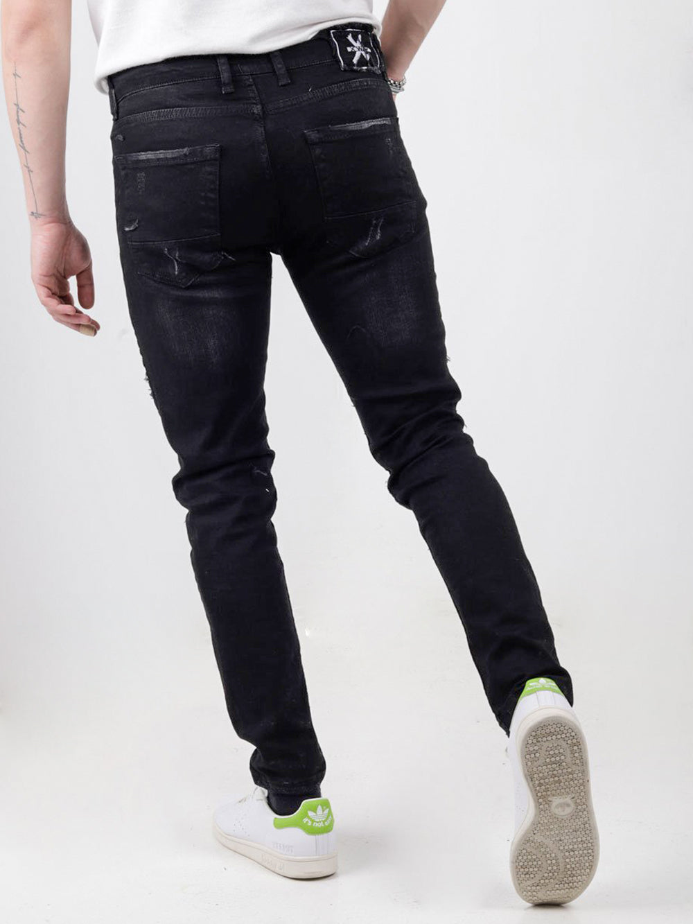 The back of a man wearing INJUN | BLACK jeans and white sneakers.