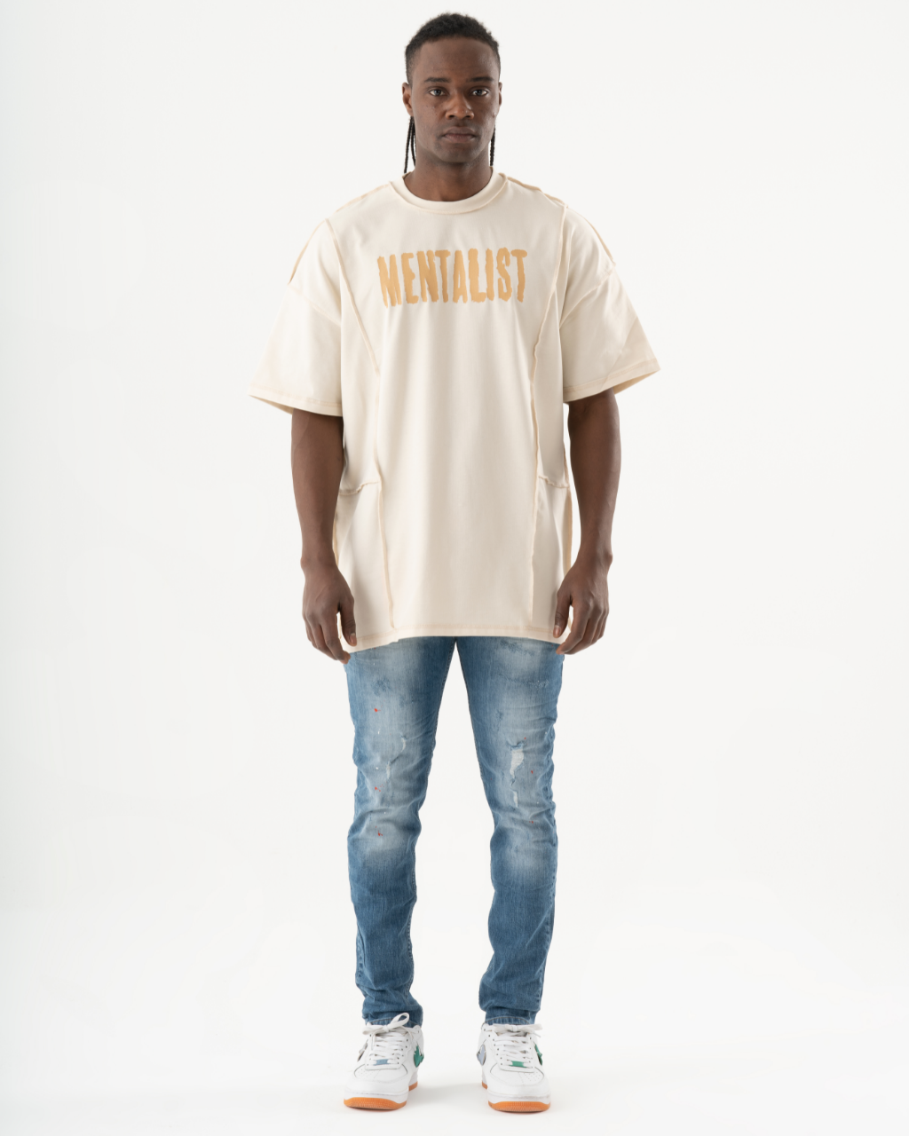 A man wearing ripped TEZAR jeans and a beige t-shirt.