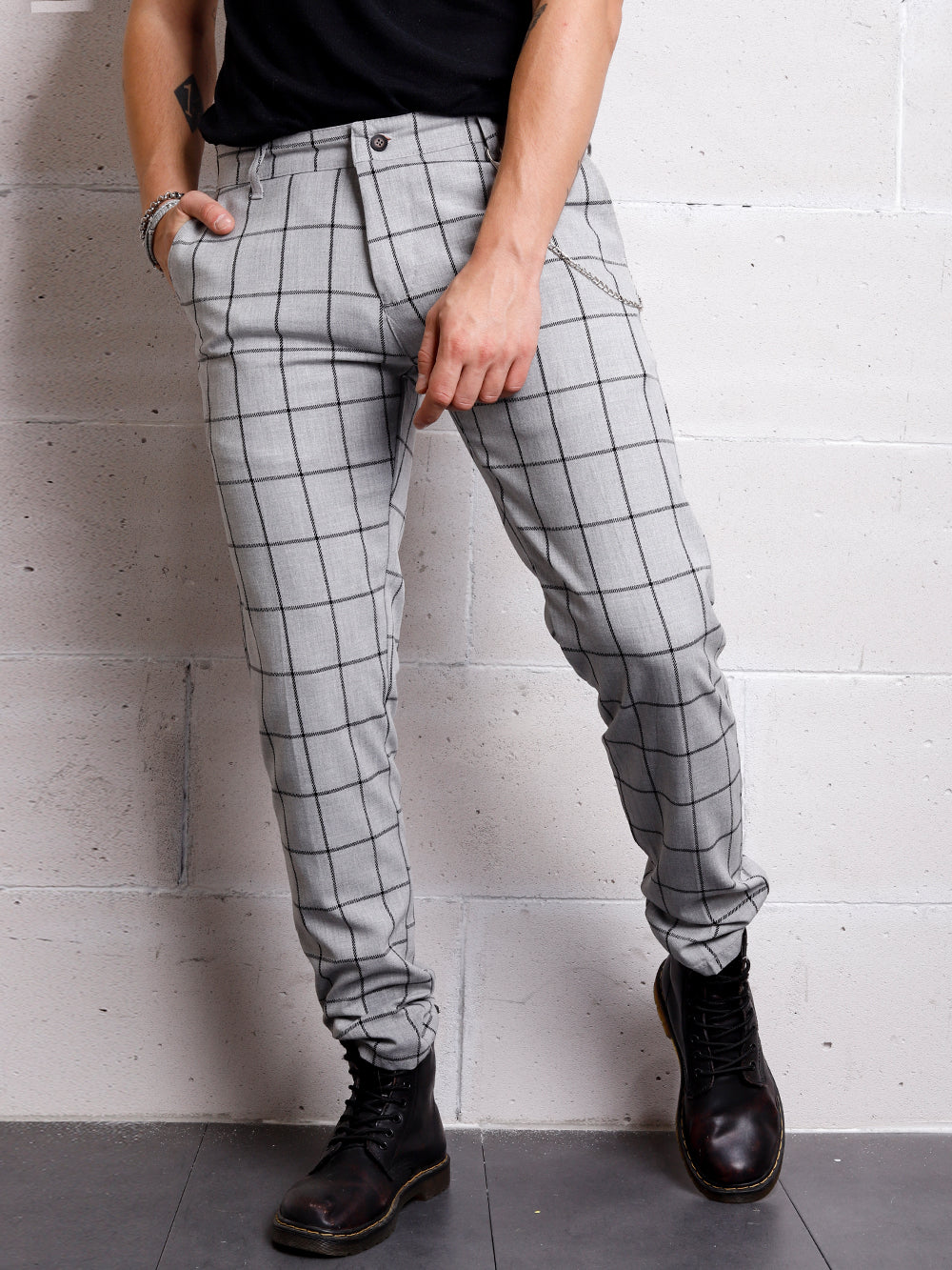 A gentleman in a black shirt and Graystone pants leaning against a wall.