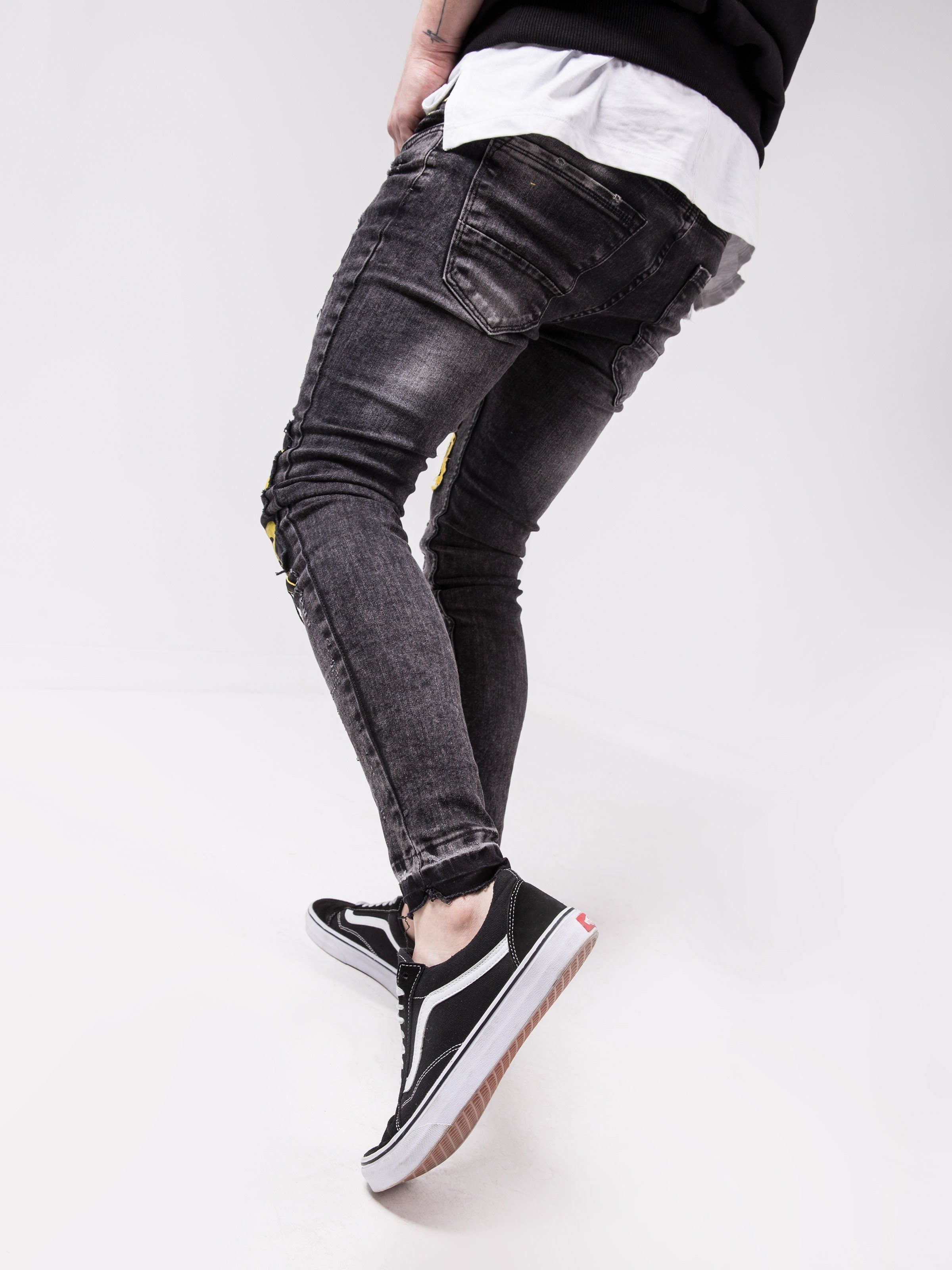 A man in MOUNT ONE jeans and sneakers is standing on a white background.