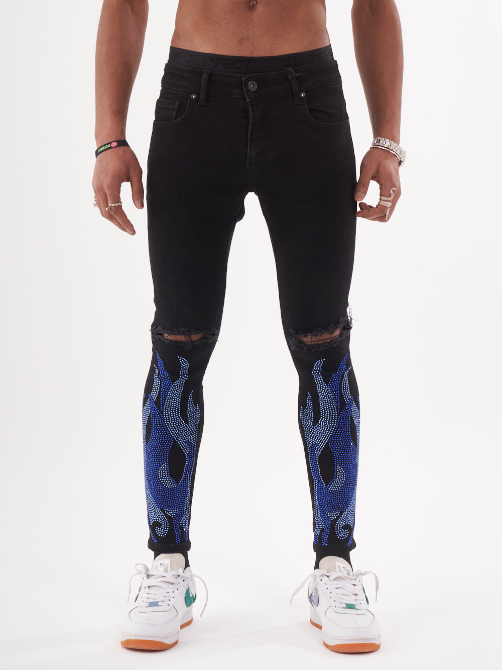 A man wearing black jeans with HELLFIRE | BLUE flames on them.