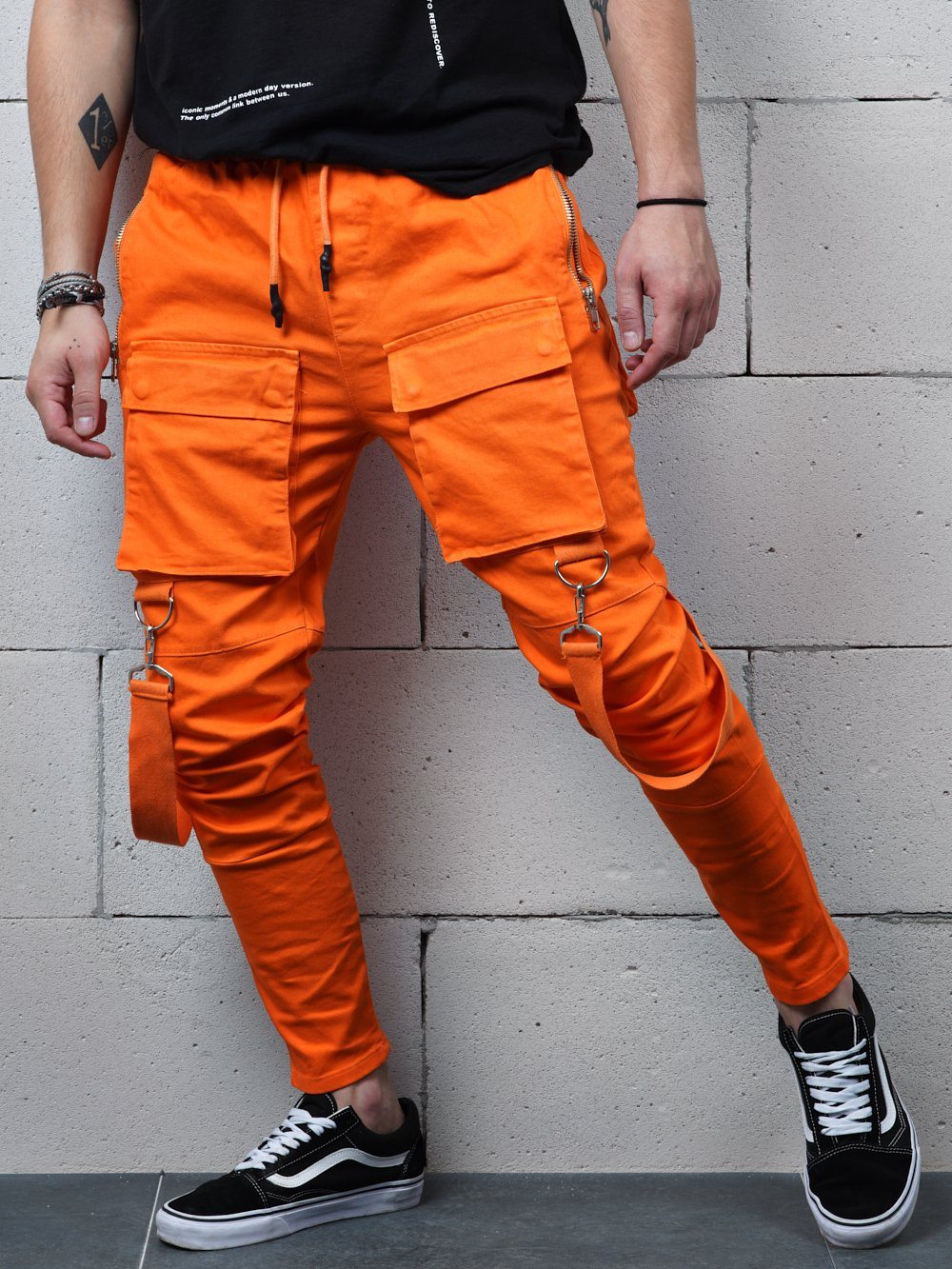 A man in ORANGE BRONX cargo pants leaning against a wall.