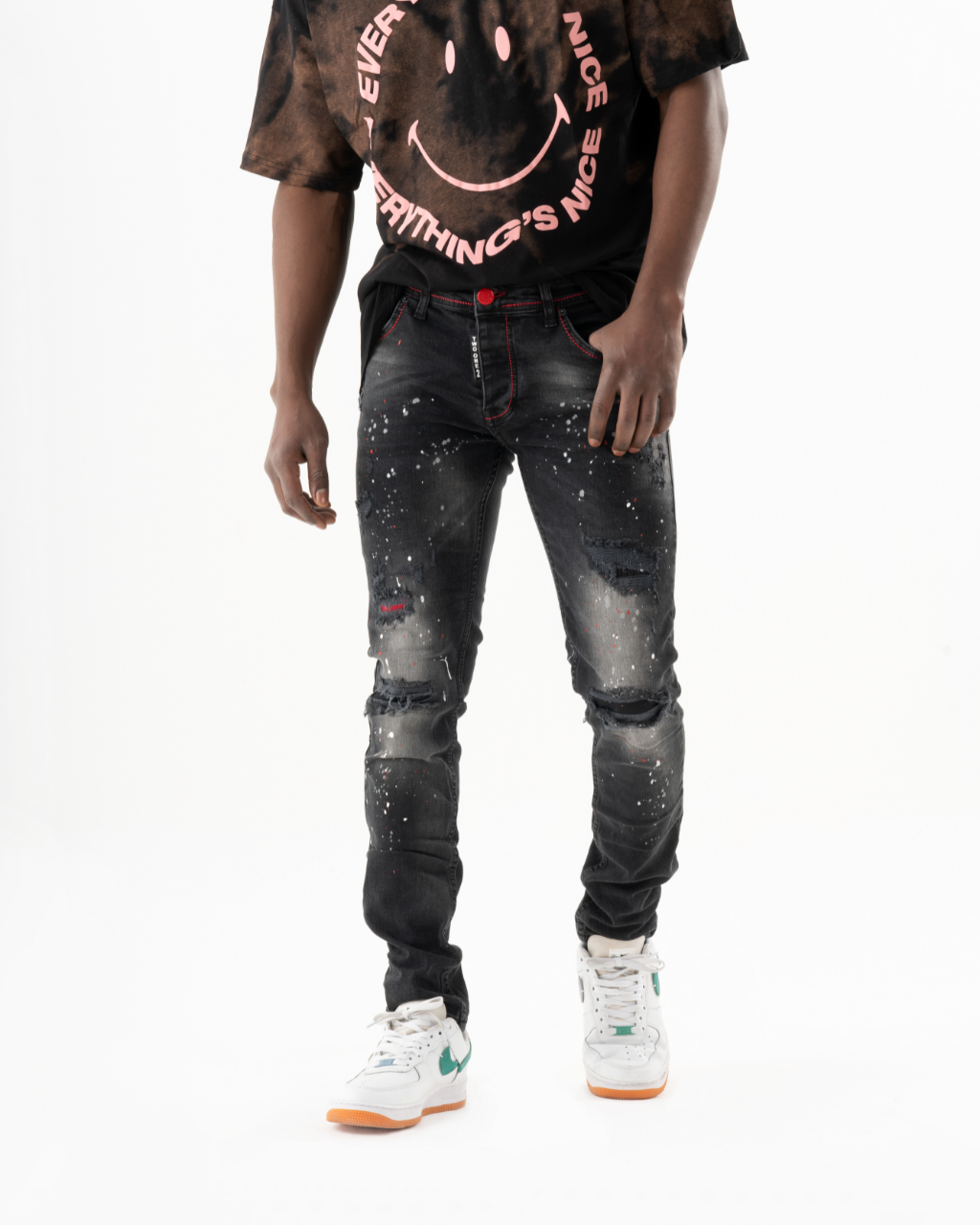 A man wearing a black t-shirt with a smiley face HOTSPOT on it and skinny fit jeans.