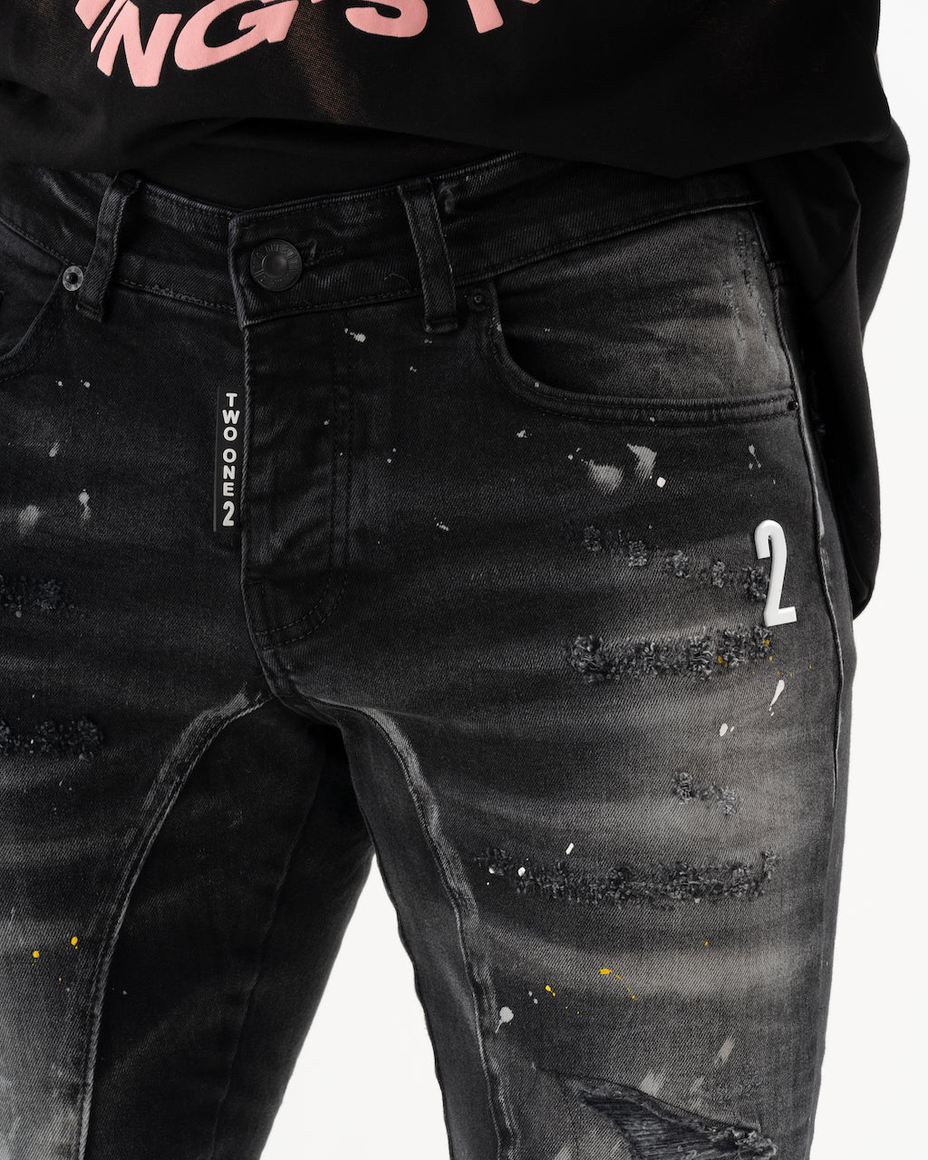 A man wearing an ENRAGE black t-shirt and jeans with elastic fabric.