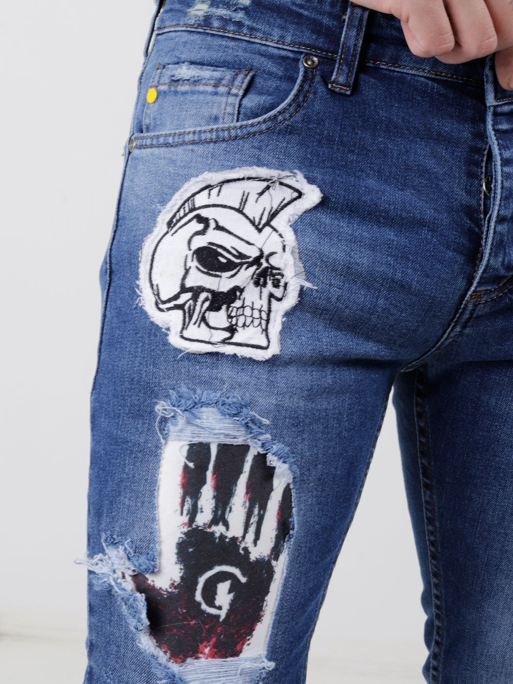 A man wearing a pair of HEADSTONE jeans with a skull patch on them.