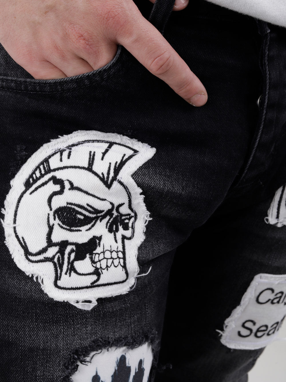A man is holding a pair of BLACK HEADSTONE jeans with a skull patch on them.
