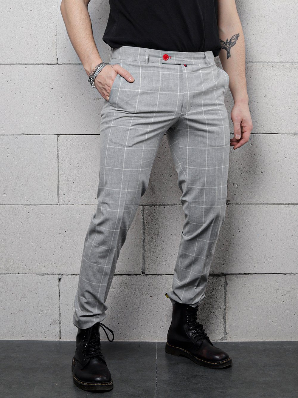 A man in ICED AMERICANO PANTS and a black shirt is posing against a wall.