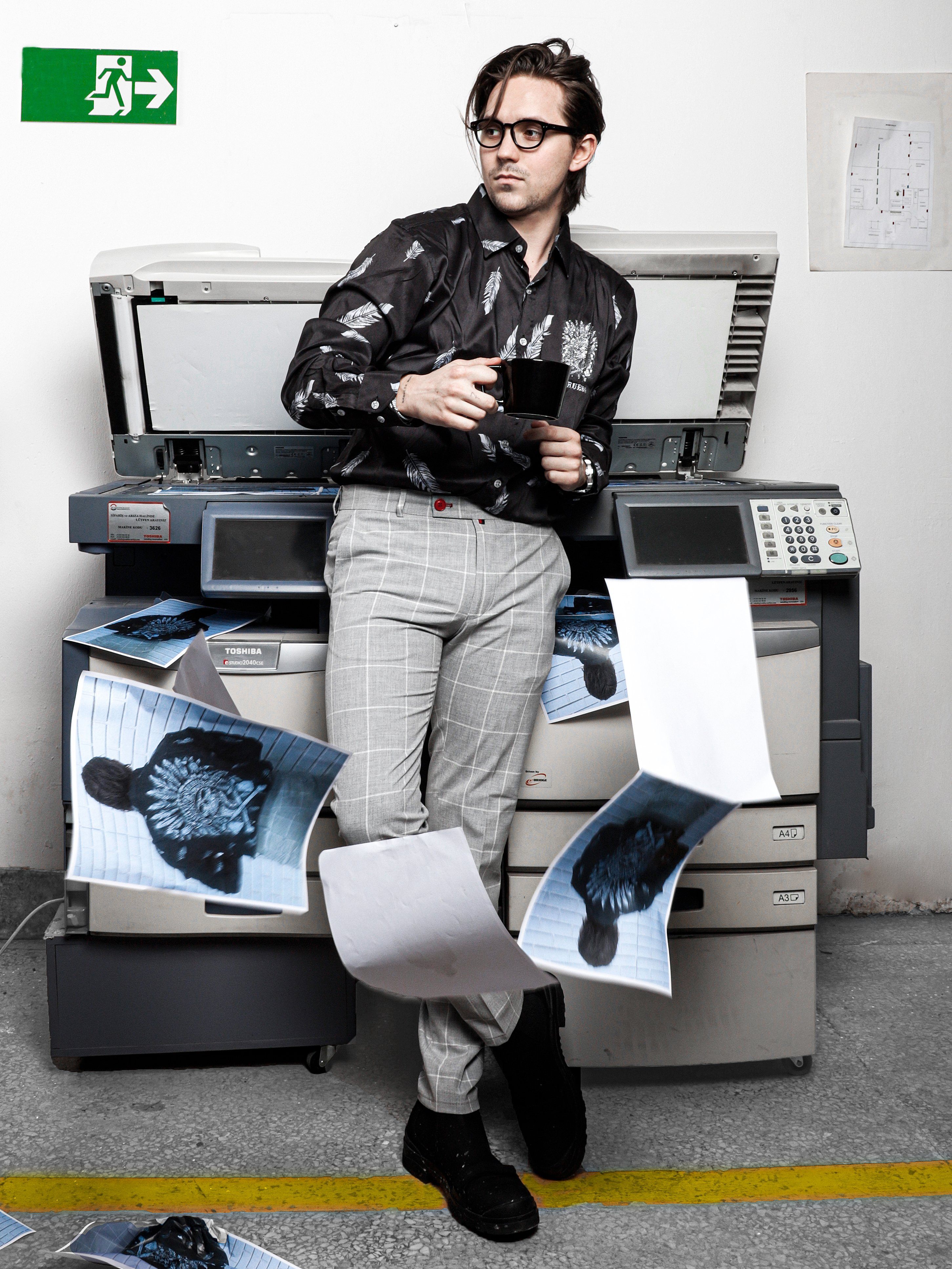 A man in ICED AMERICANO PANTS standing in front of a printer.
