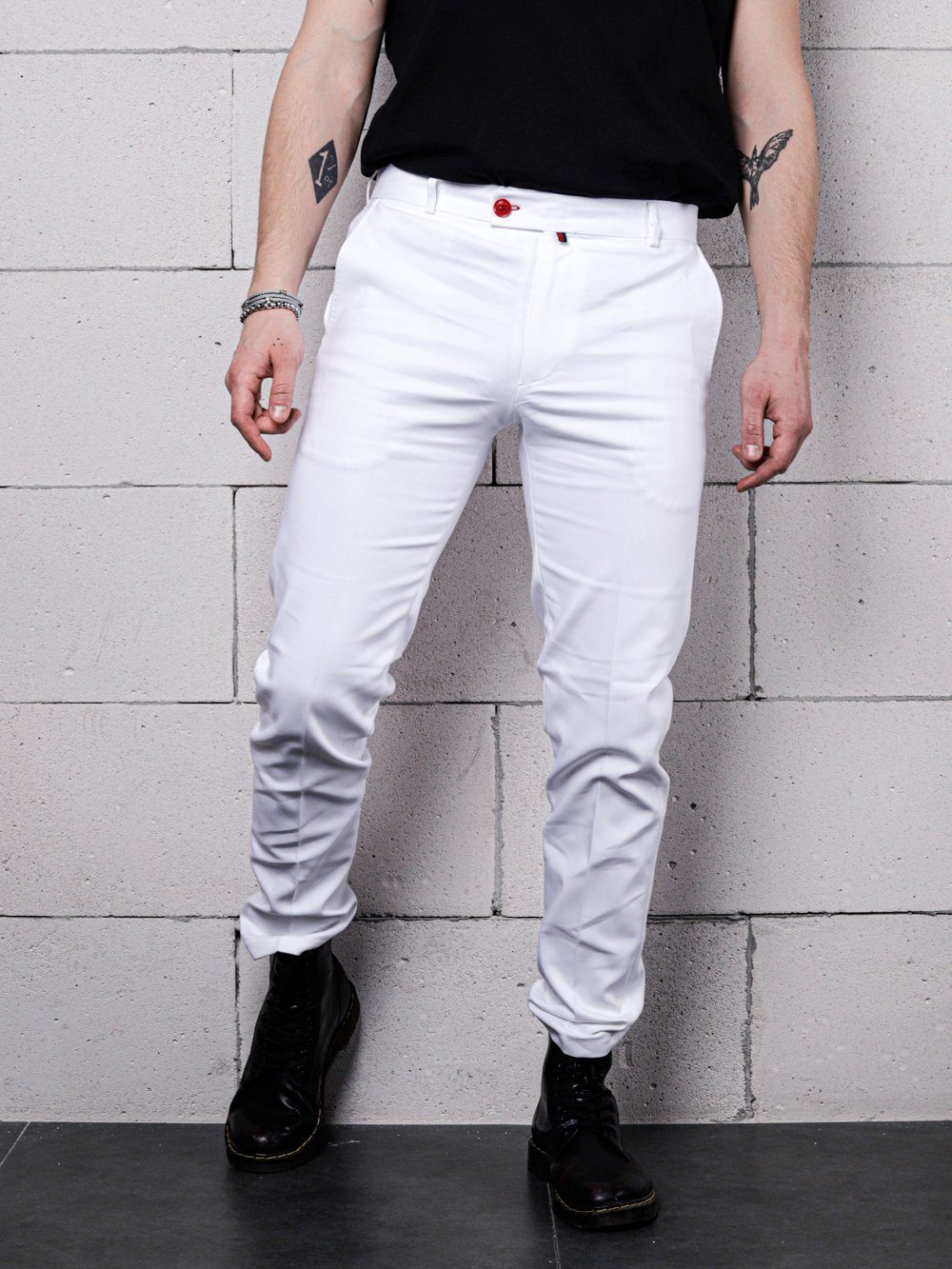 A man in a black shirt and CREAM FRAPPUCCINO PANTS leaning against a brick wall.