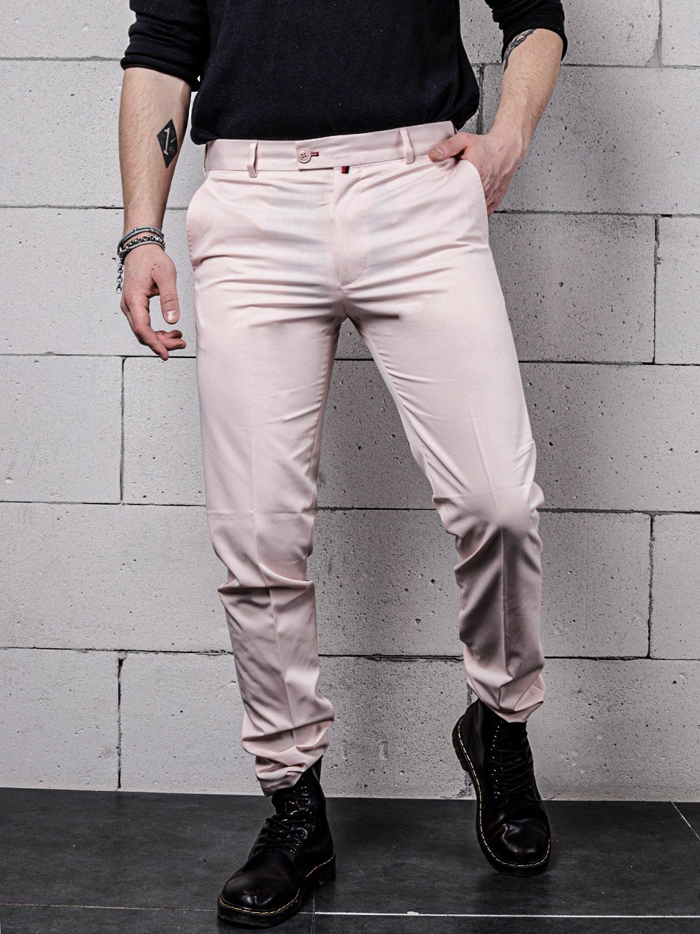 A man in CANDY DUST PANTS is standing against a brick wall.