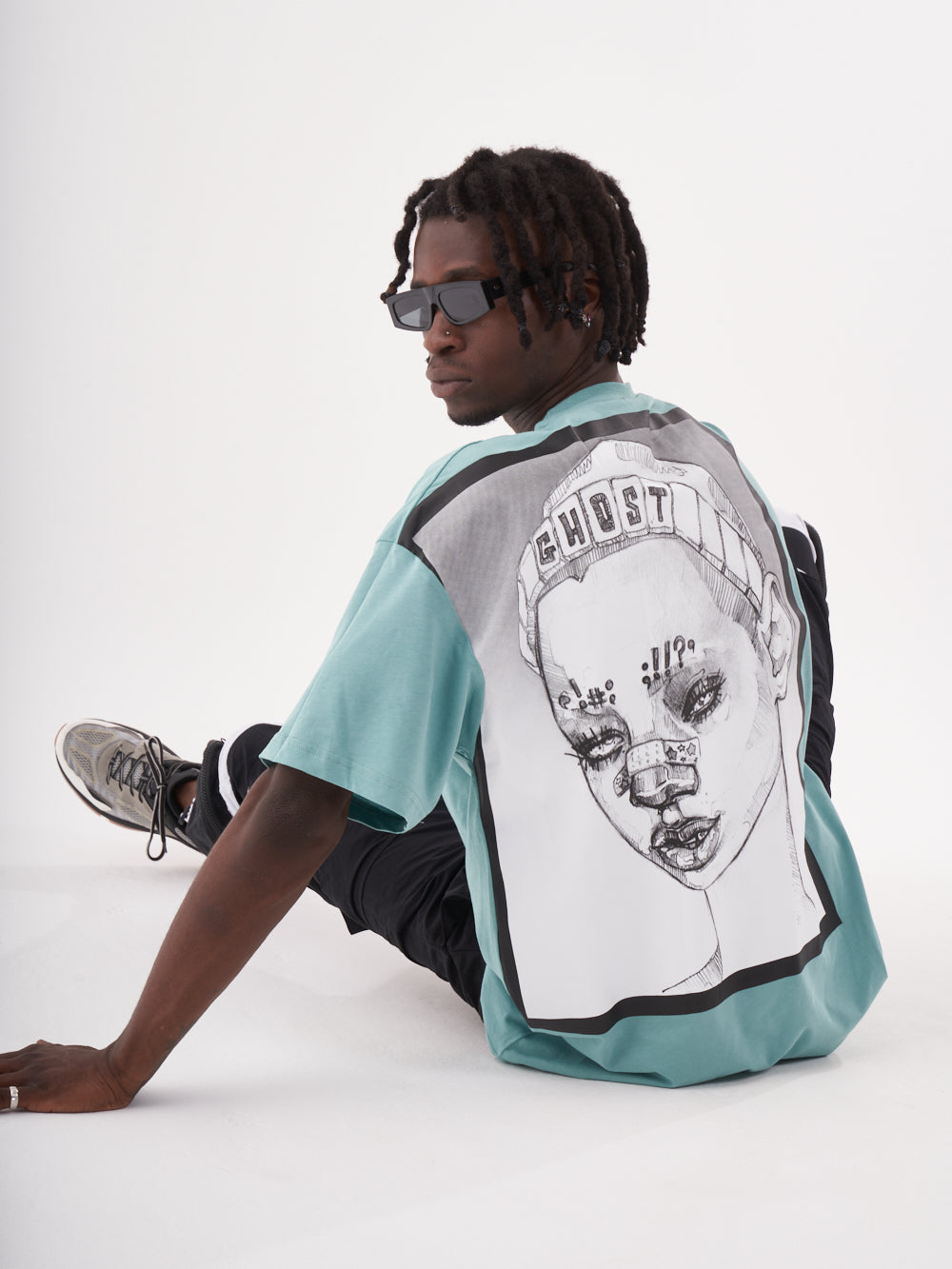 A man sitting on the ground wearing a GHOST T-SHIRT with a drawing of a woman.