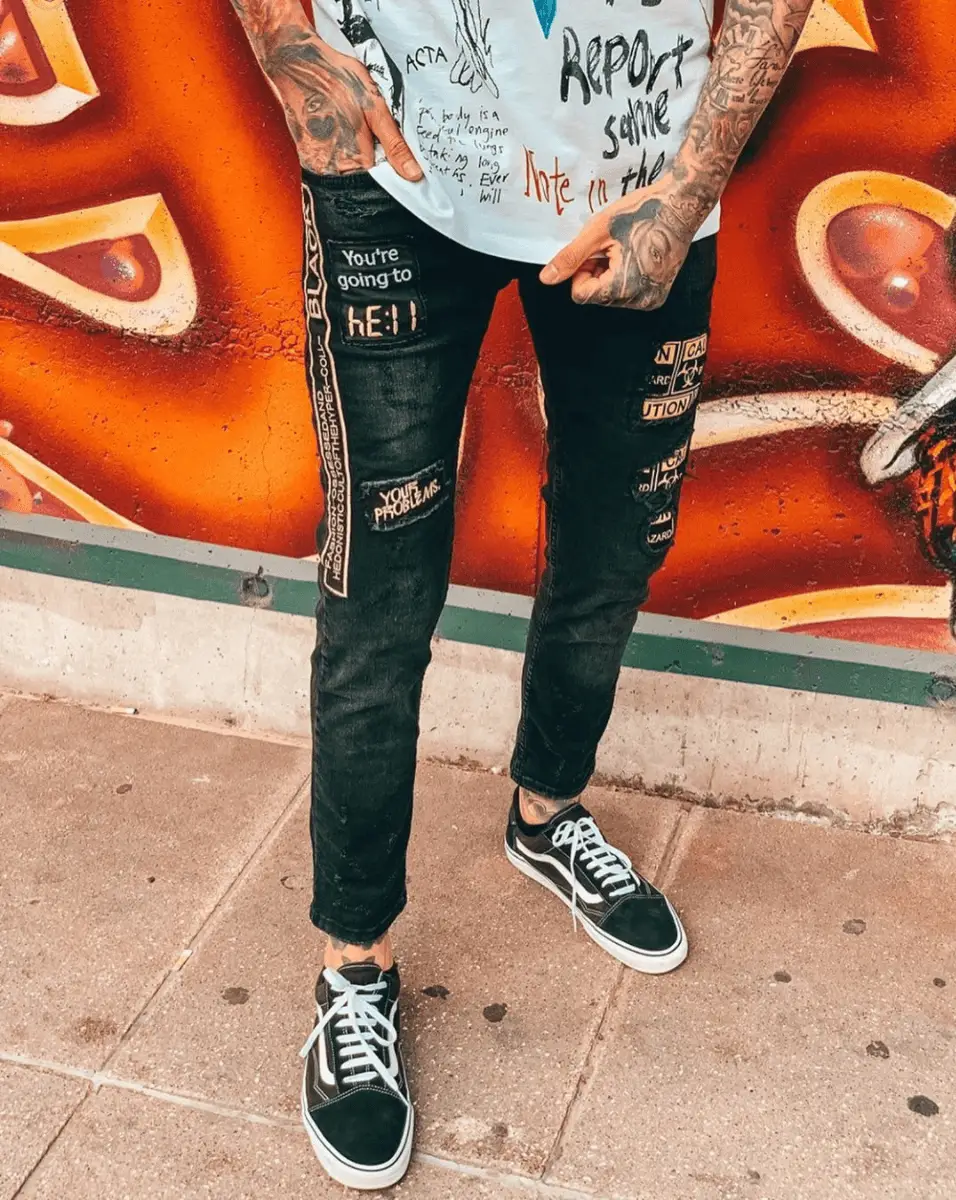 A man wearing a BLACK FALCON t-shirt and jeans standing in front of a graffiti wall.