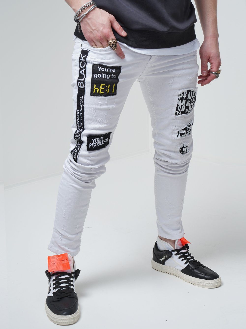 A man wearing WHITE FALCON jeans with patches on them.