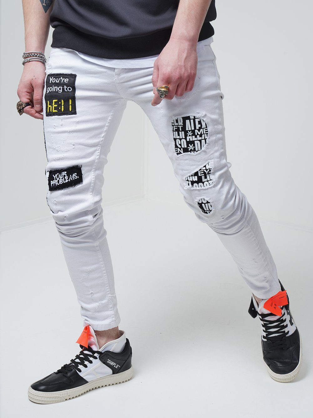 A man wearing WHITE FALCON jeans with patches on them.