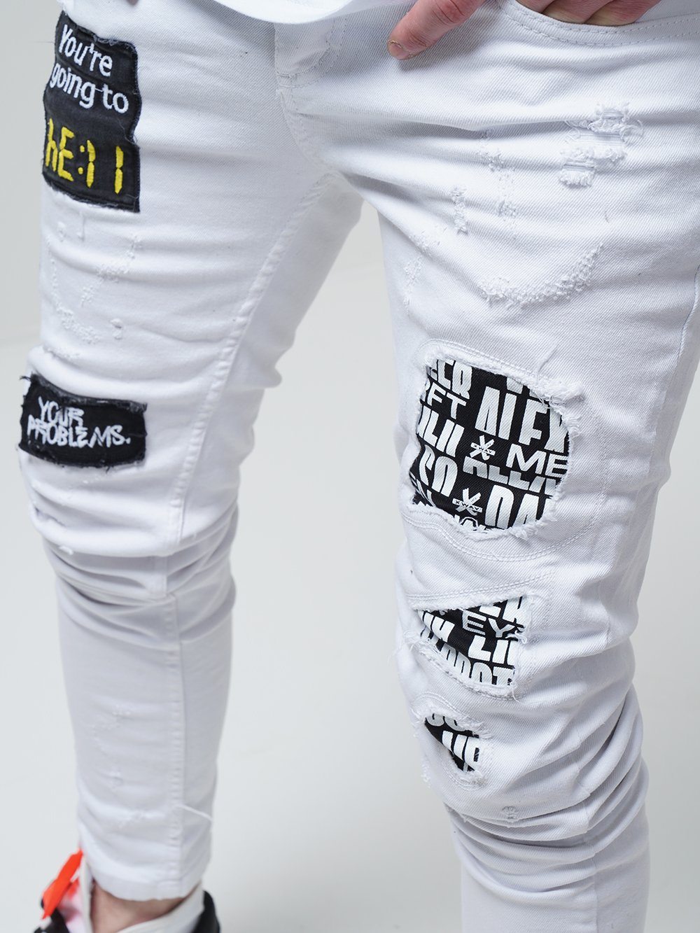 A man wearing WHITE FALCON jeans with patches on them.