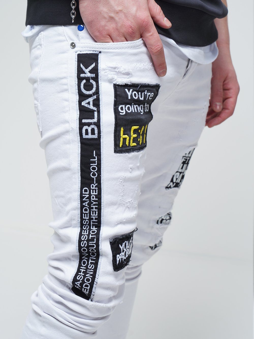 A man wearing a pair of WHITE FALCON jeans with black patches on them.