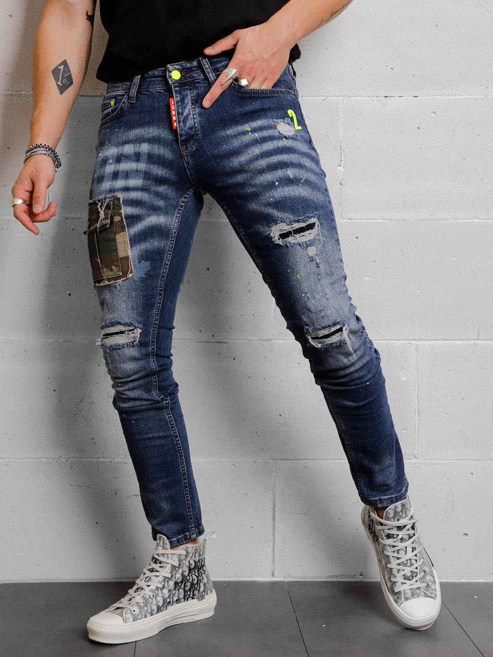 A man wearing ripped jeans and a CAMOUFLAGE | BLUE t - shirt.