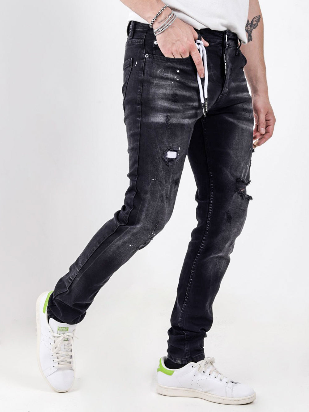 A man wearing black jeans and white MODERO sneakers.