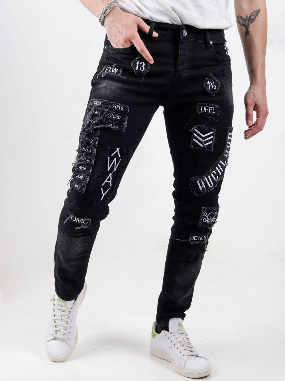 A man wearing INJUN | BLACK jeans with patches on them.