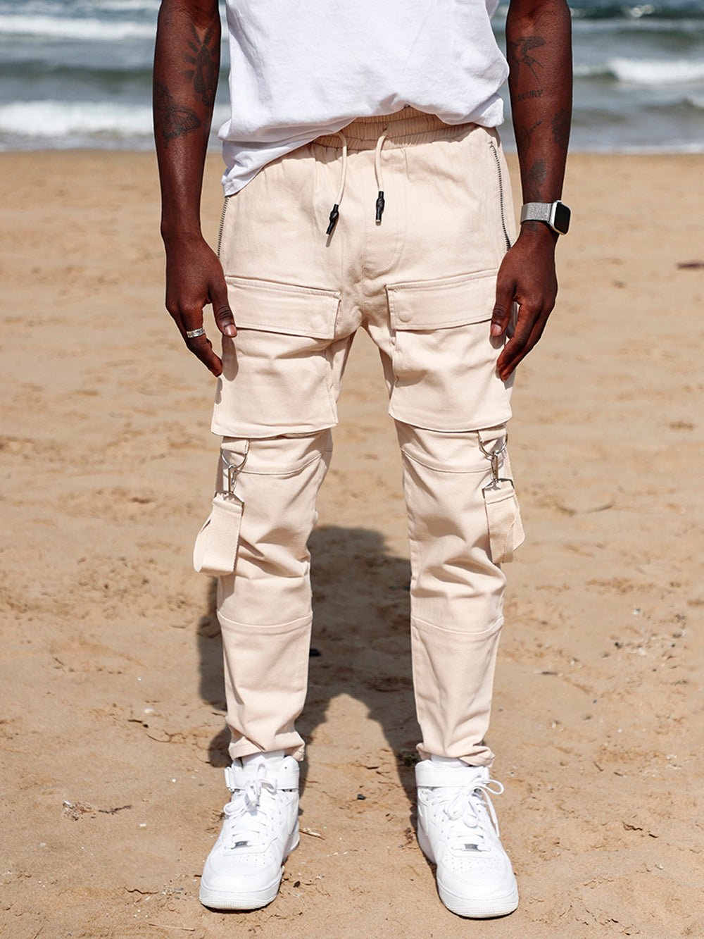 A man standing on the beach wearing BEIGE BRONX Jogger pants with cargo pockets, combining style and function.