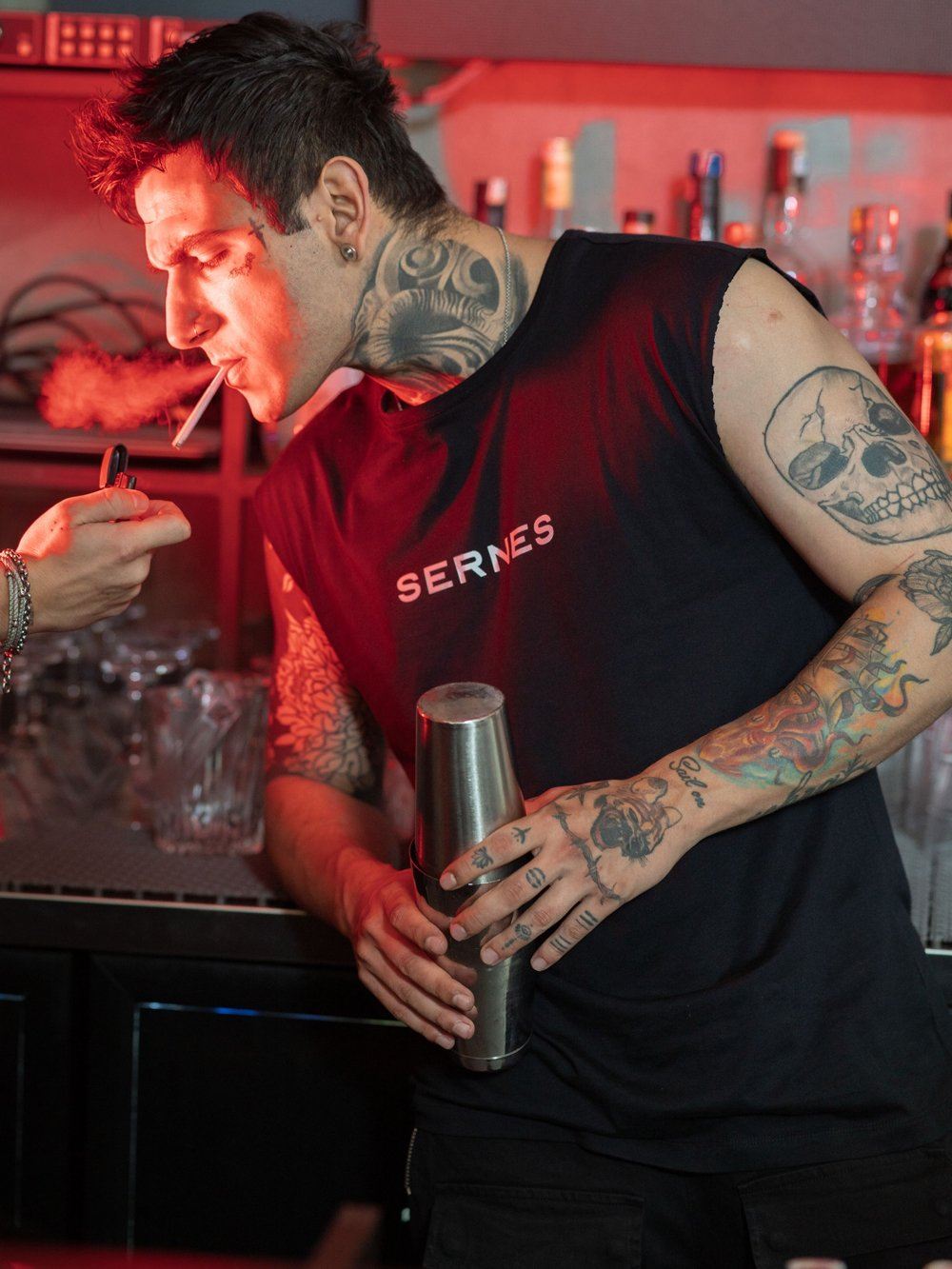 A man smoking a THE ORIGINAL T-SHIRT in a bar.