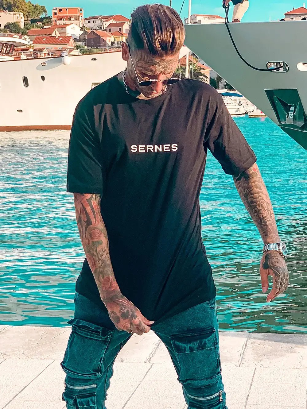 A man wearing THE ORIGINAL T-SHIRT standing next to a boat.