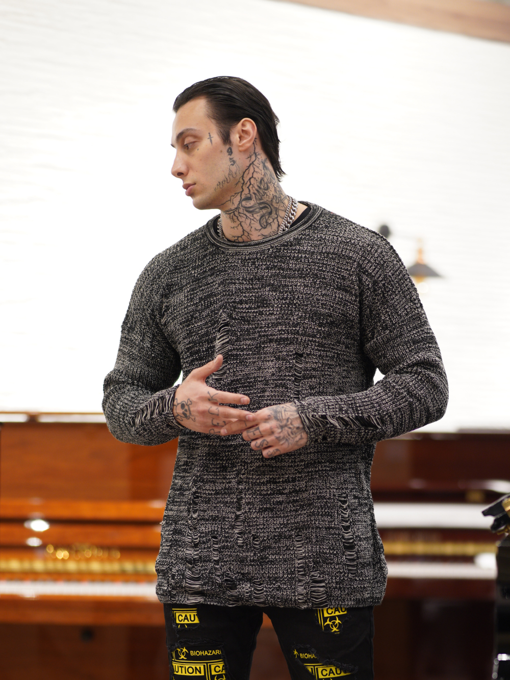A man wearing a Distressed Gentleman Sweater | Gray standing in front of a piano.