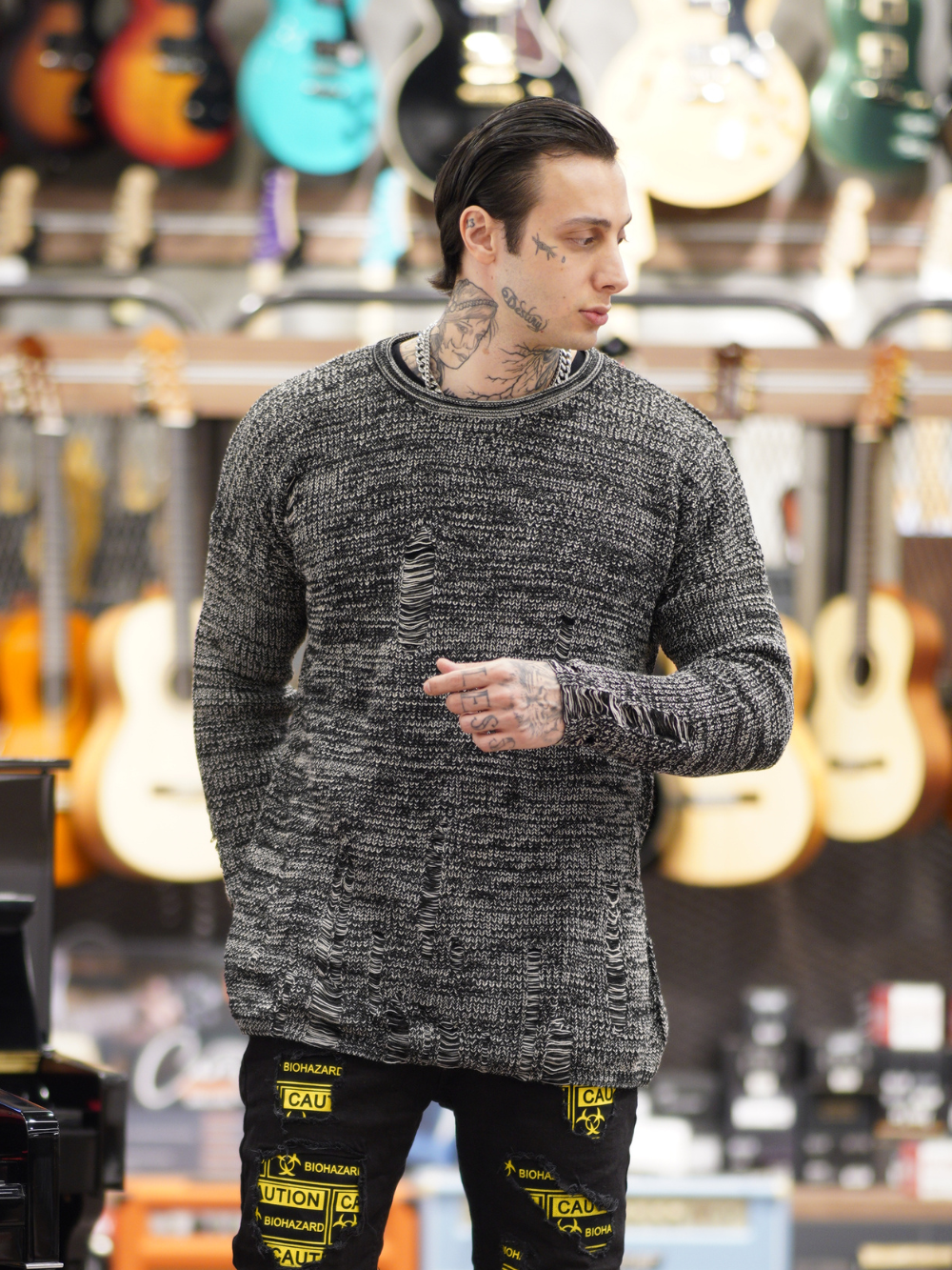 A distressed man with tattoos standing in front of a Distressed Gentleman Sweater shop.