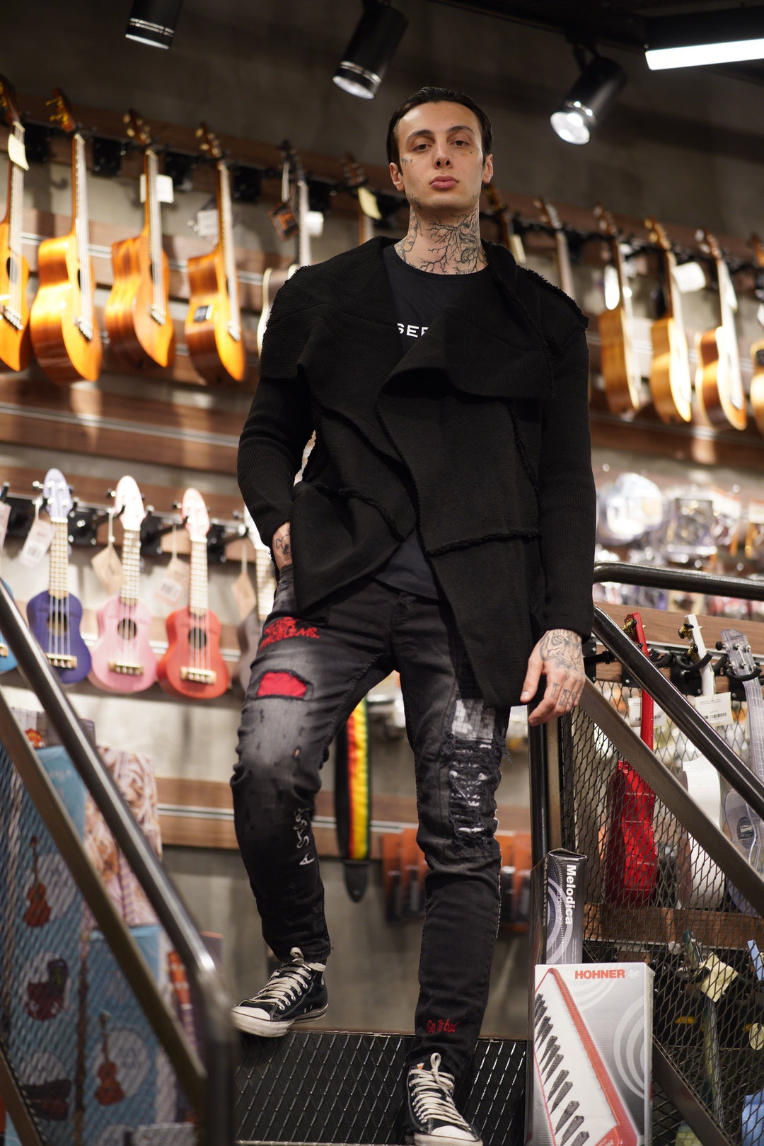 A man in a black HOODED DISTRESSED CARDIGAN // BLACK, the perfect fit for his size, standing in a music store.