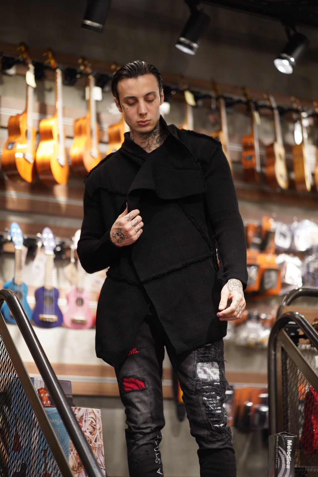 A man in a black HOODED DISTRESSED CARDIGAN, fitting perfectly, standing in a store.