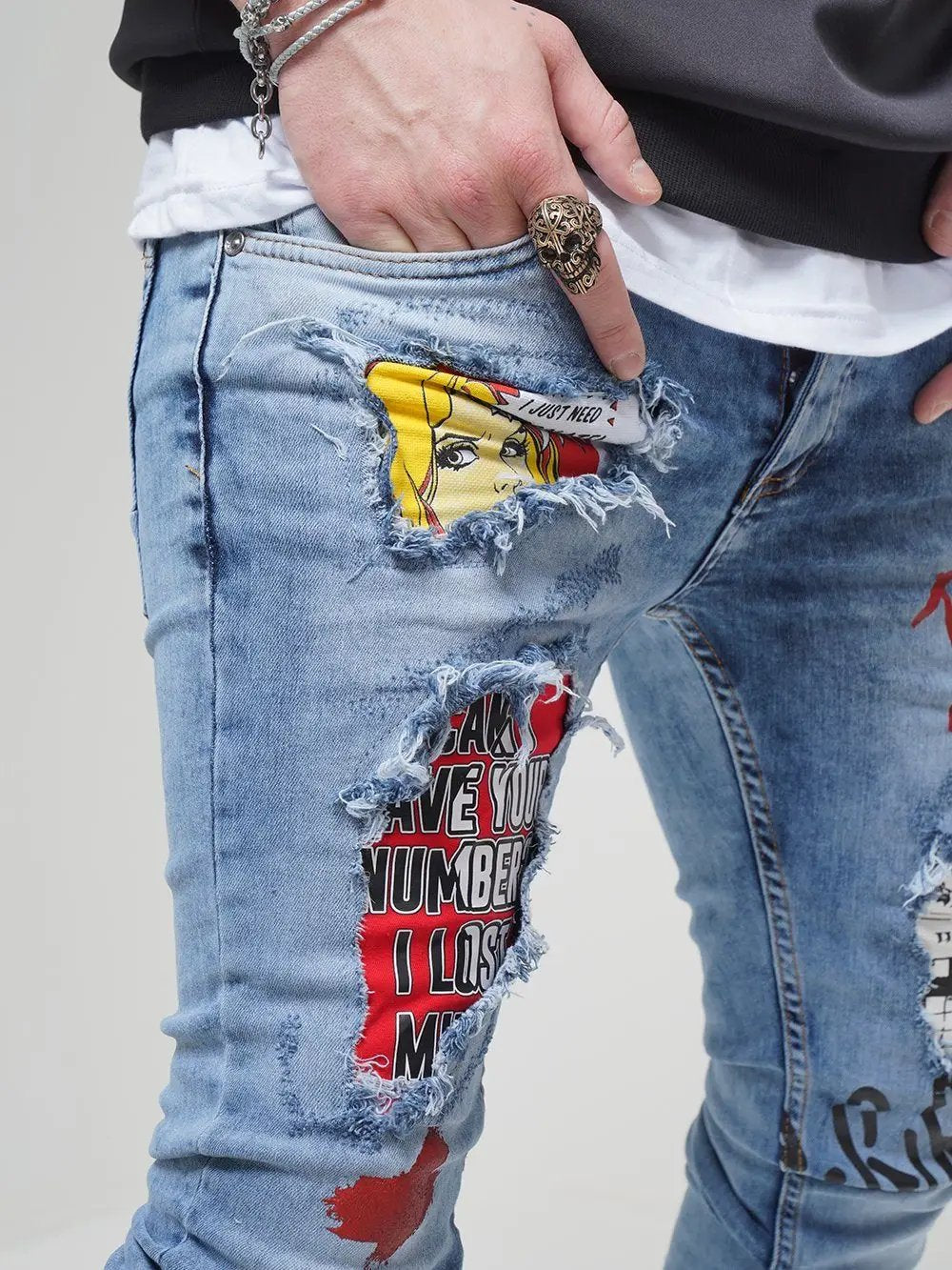 A man wearing ripped jeans with BANKSY graffiti on them.
