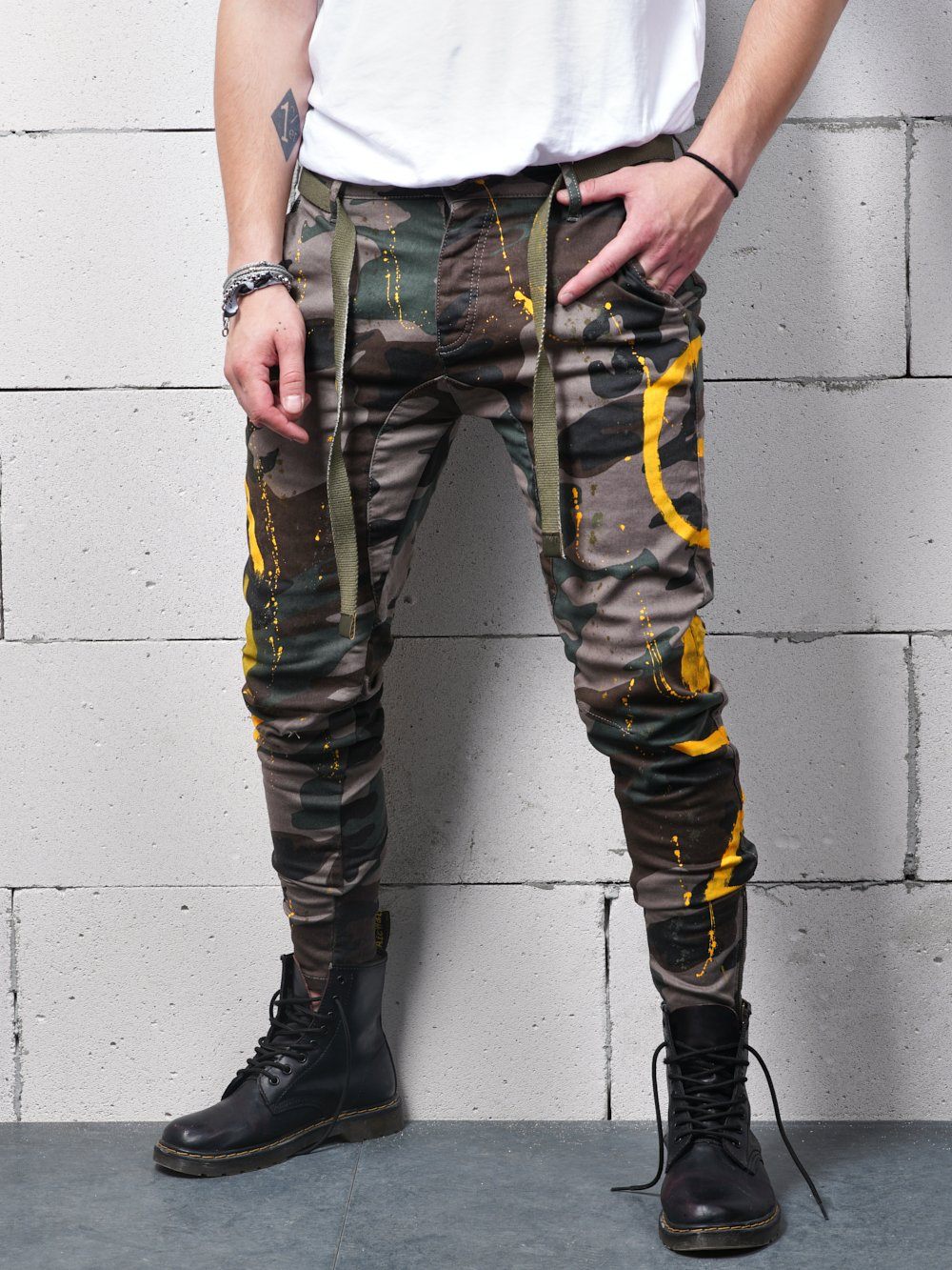 A man in camouflage pants wearing KONGOS stands against a wall.
