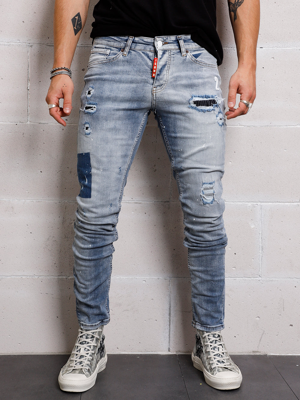 A man wearing SKY BLUE ICON DENIM distressed ripped jeans and a black t-shirt.