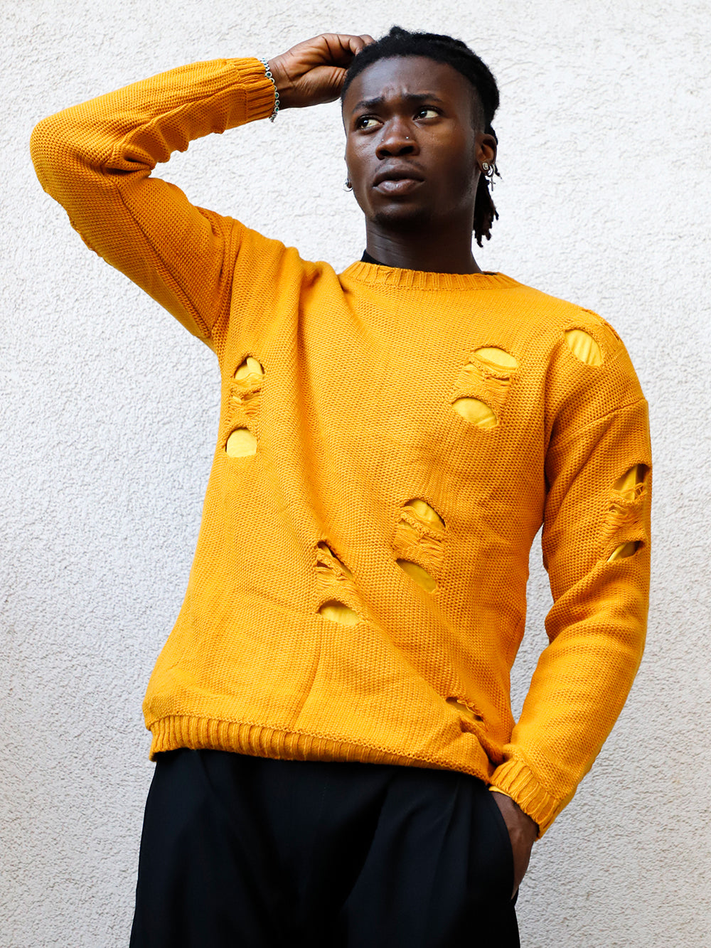 A man in a yellow DISTRESSED DOUBLE LAYER SWEATER // MUSTARD is leaning against a wall.